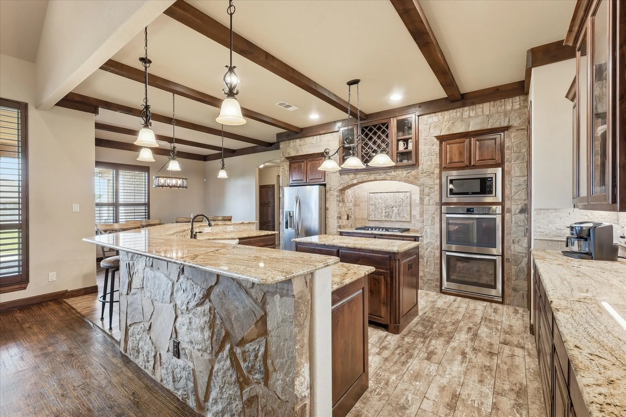 Spacious kitchen featuring stone accent walls, natural wood-finish flooring, and exposed ceiling beams