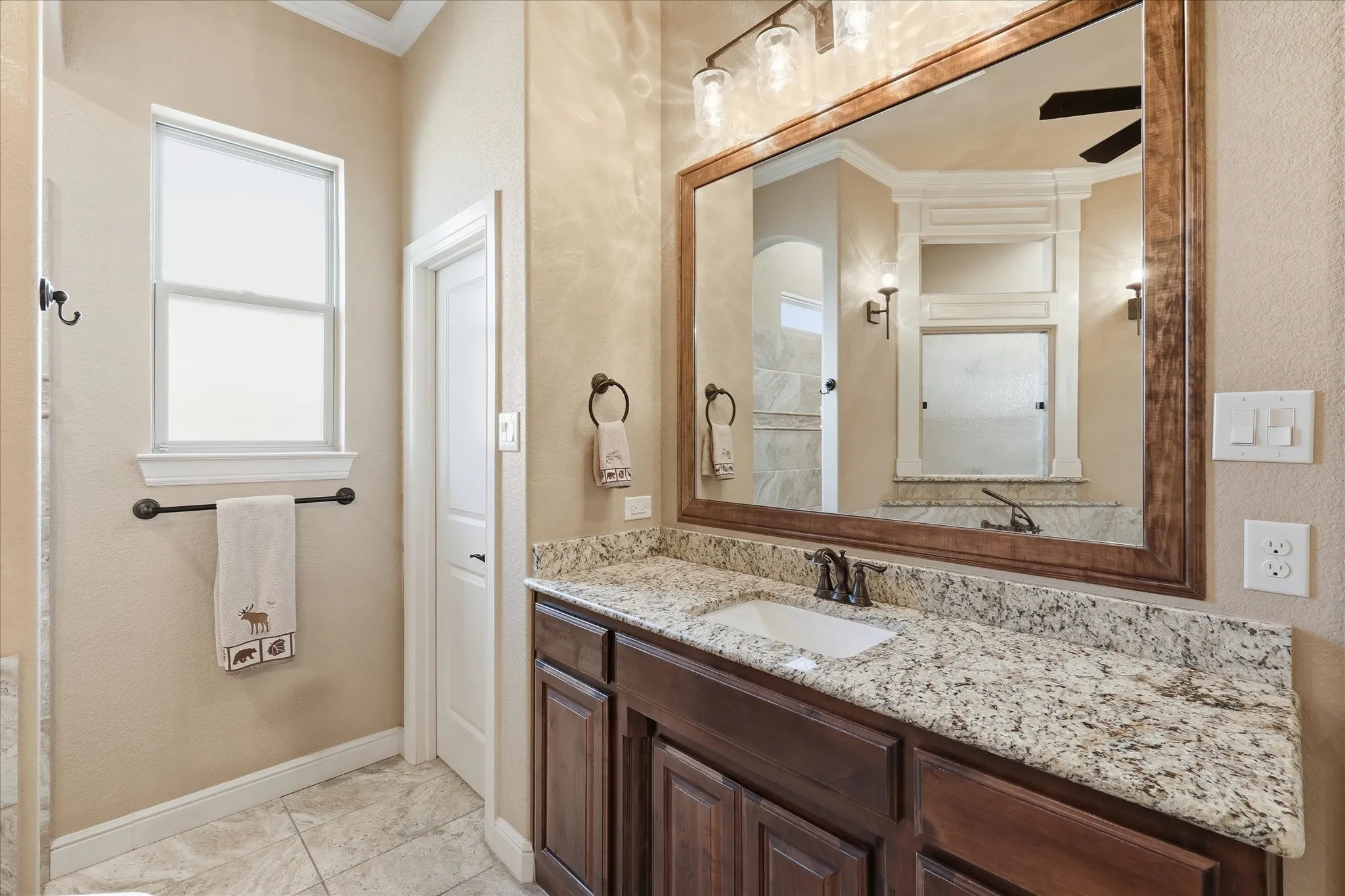 Bathroom vanity featuring granite countertop, undermount sink, wood-finish cabinetry, and a framed mirror