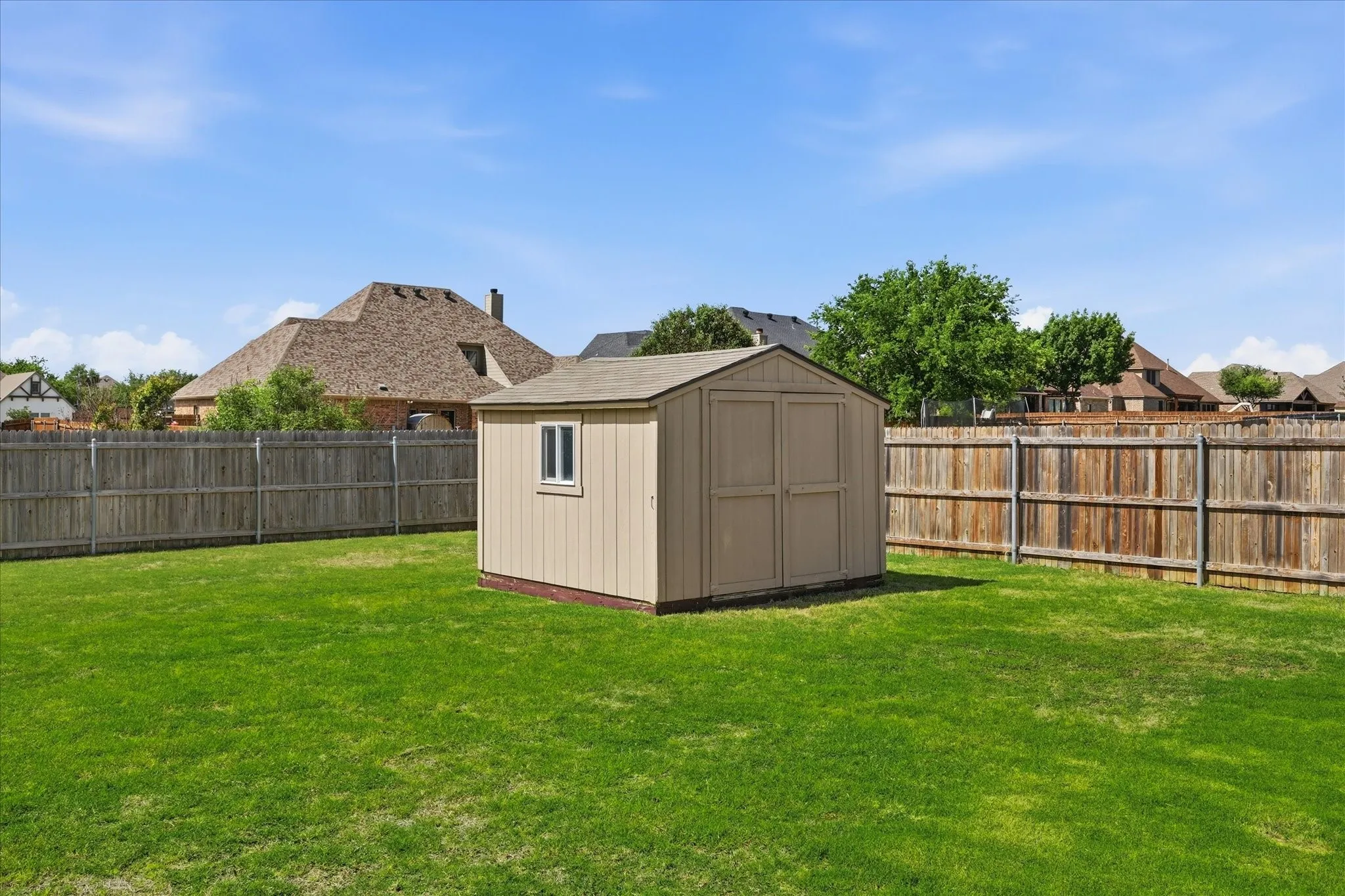Expansive green lawn featuring a tan storage shed with a white-framed window and double doors