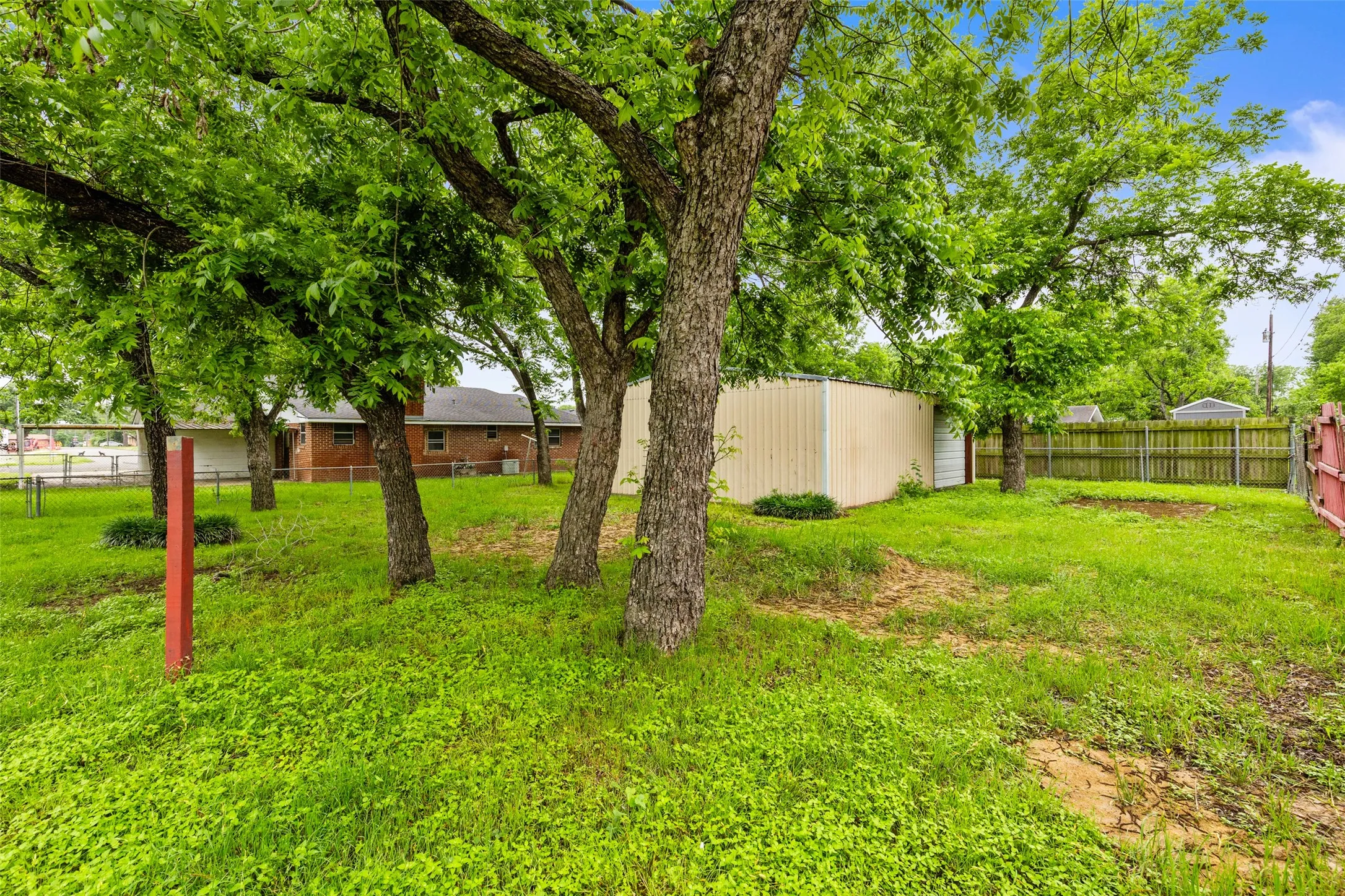 Expansive exterior area featuring mature trees, a detached storage building, and a wood privacy fence