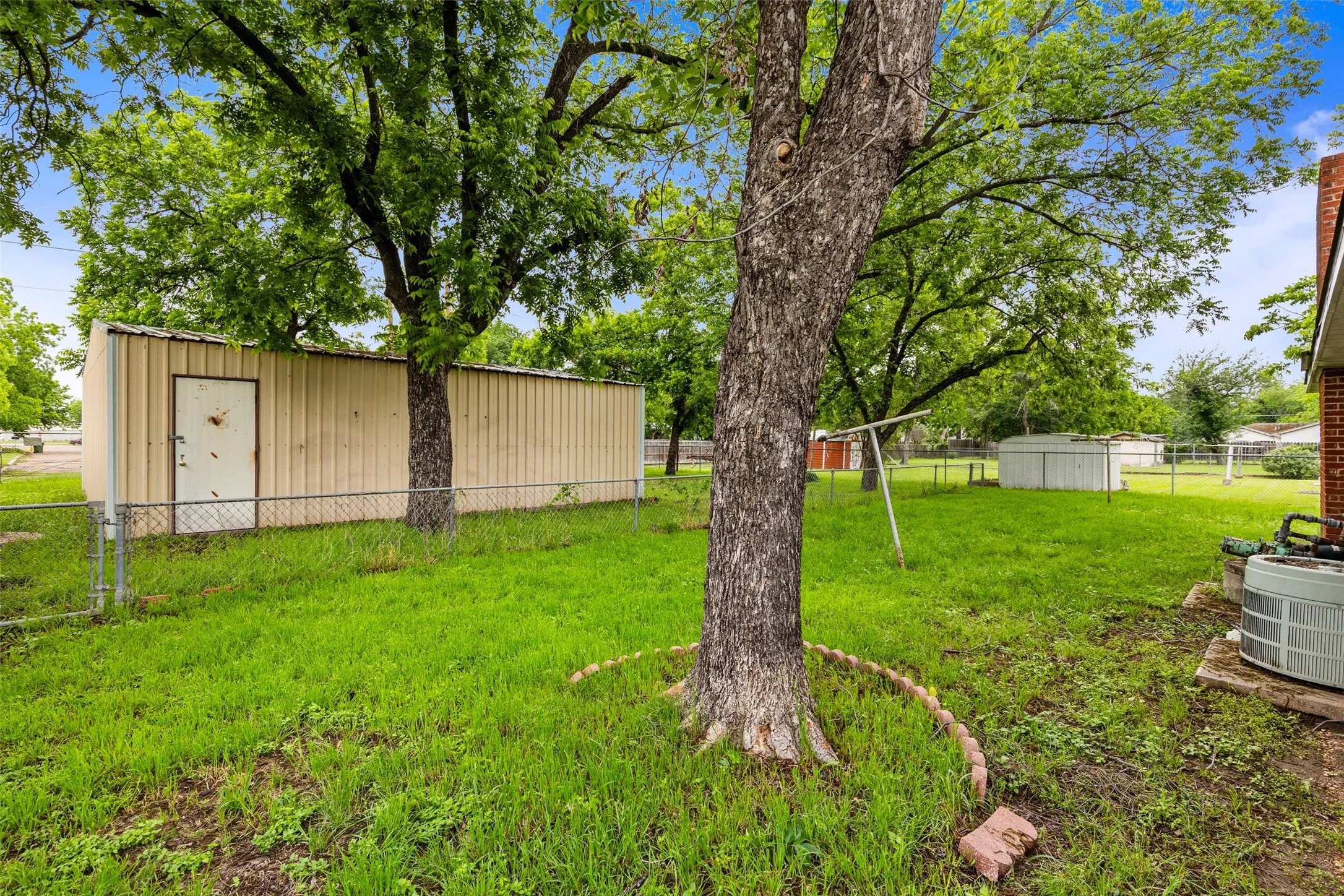 Expansive grassy yard area featuring mature trees and a long storage shed with a single entry door