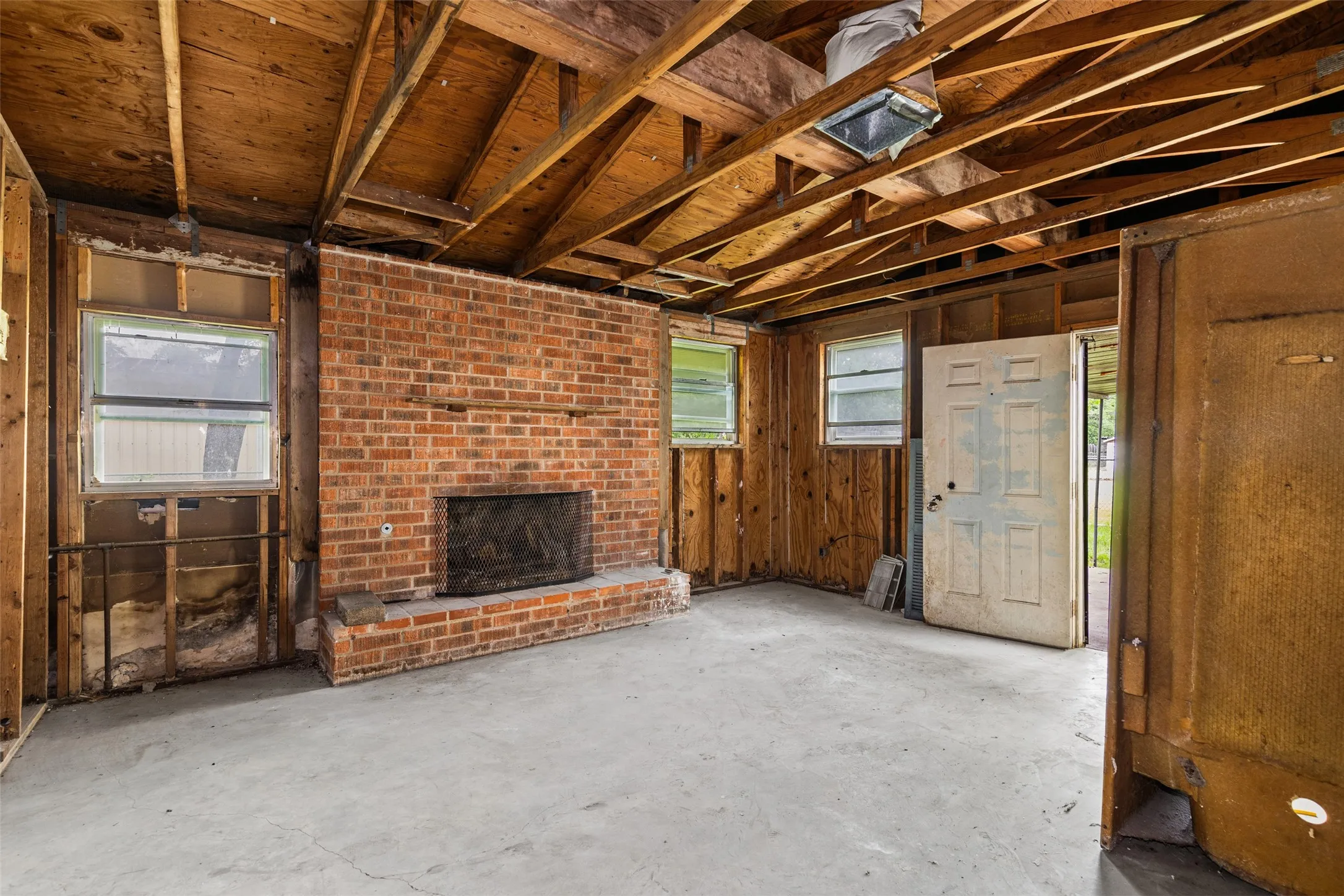 Exposed wood beam ceiling with an open floor plan, brick fireplace, and multiple window openings
