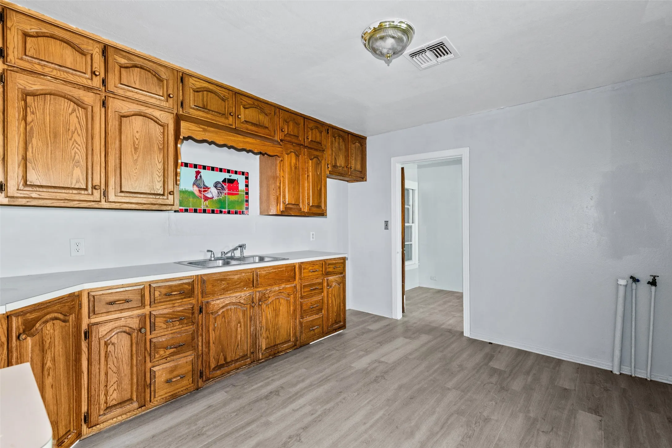 Kitchen featuring extensive wood cabinetry, light-toned countertops, a double basin stainless steel sink with a chrome faucet, and wood-finish flooring