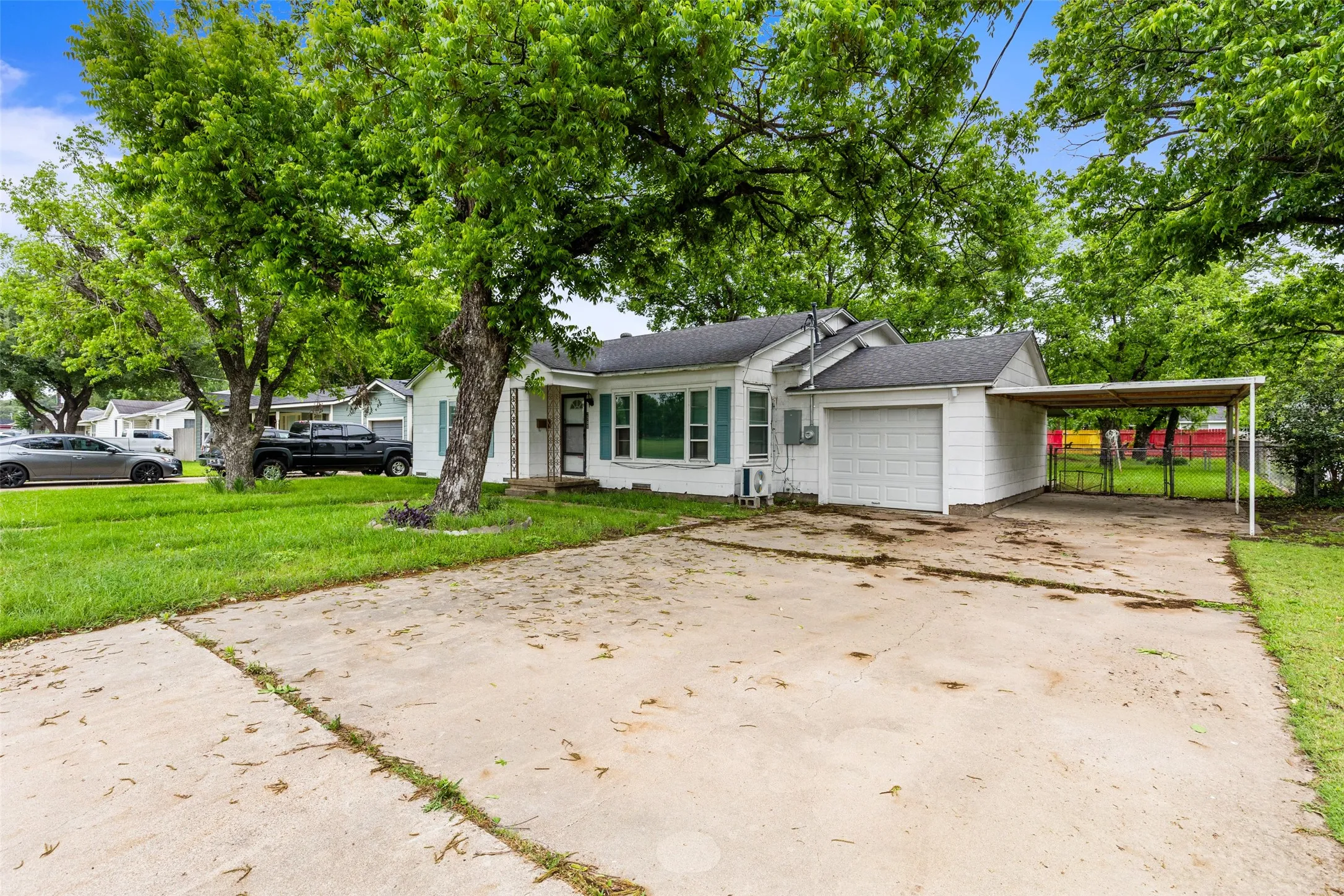 White exterior with teal window shutters, an attached garage, a carport, and a concrete driveway