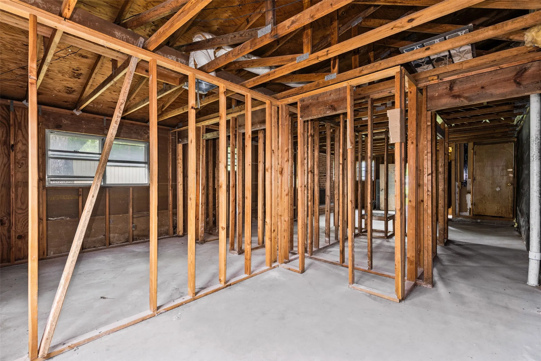 Interior framing showcasing structural wood beams, exposed plywood subfloor, concrete slab flooring, and multiple window openings