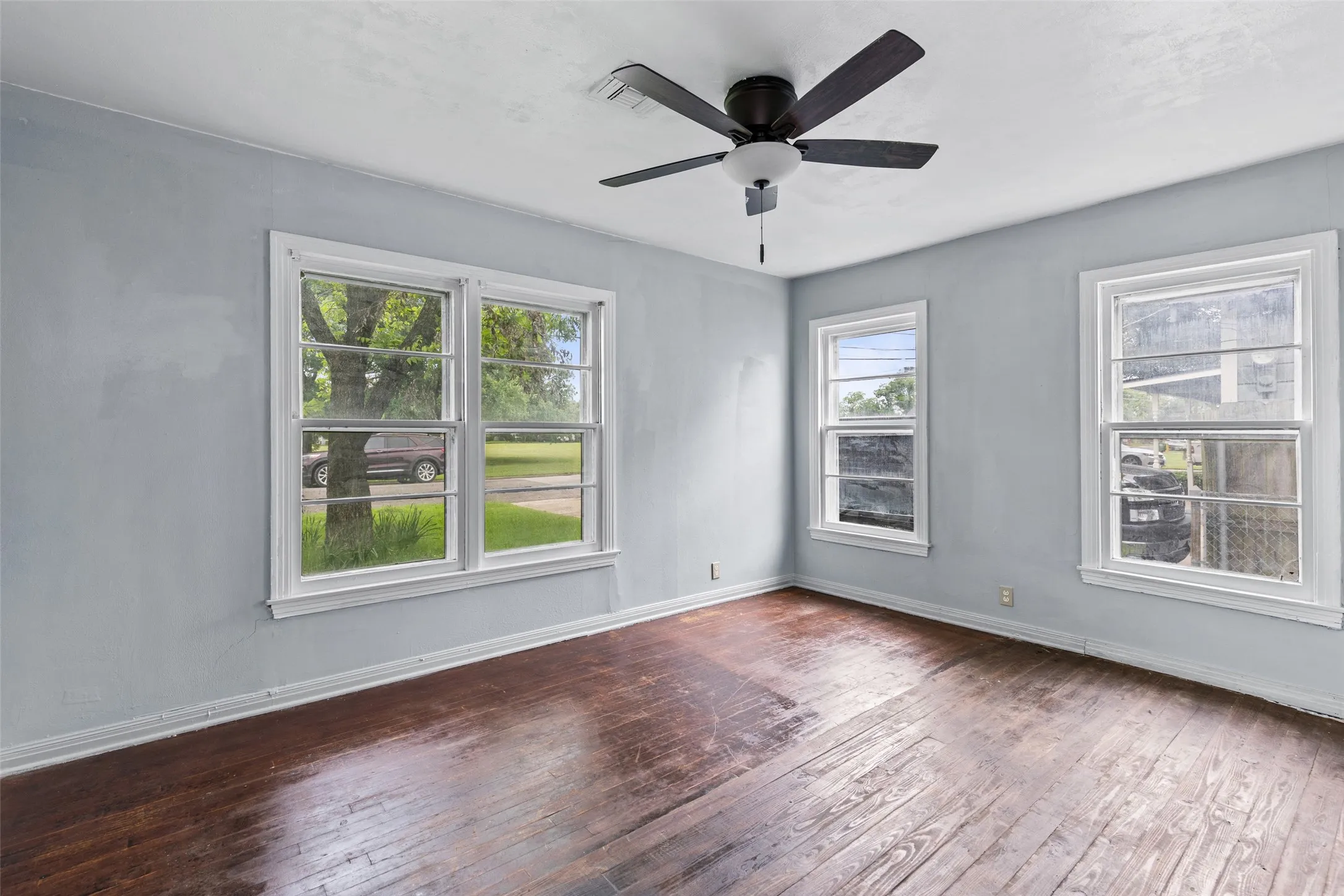 Room featuring wood-finish flooring, light blue wall paint, a ceiling fan with integrated lighting, and multiple windows with white trim