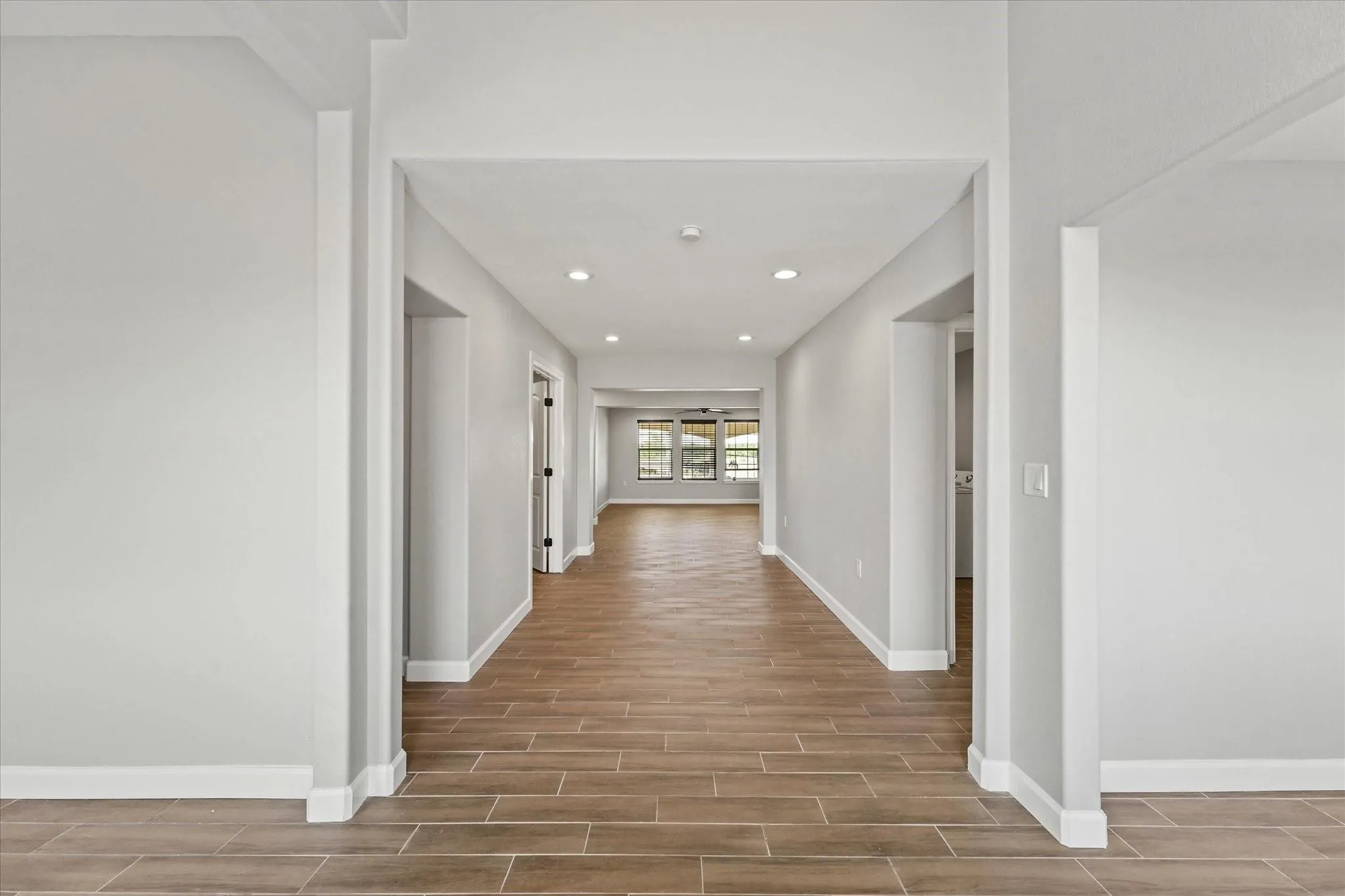 Spacious hallway featuring wood-finish flooring, recessed lighting, neutral wall tones, and white trim throughout