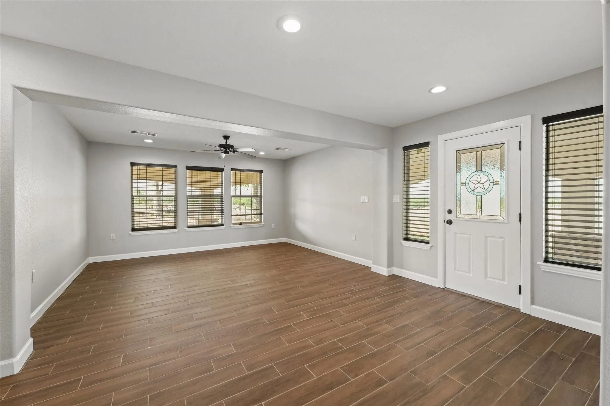 Spacious living area featuring wood-finish tile flooring, recessed lighting, and a ceiling fan