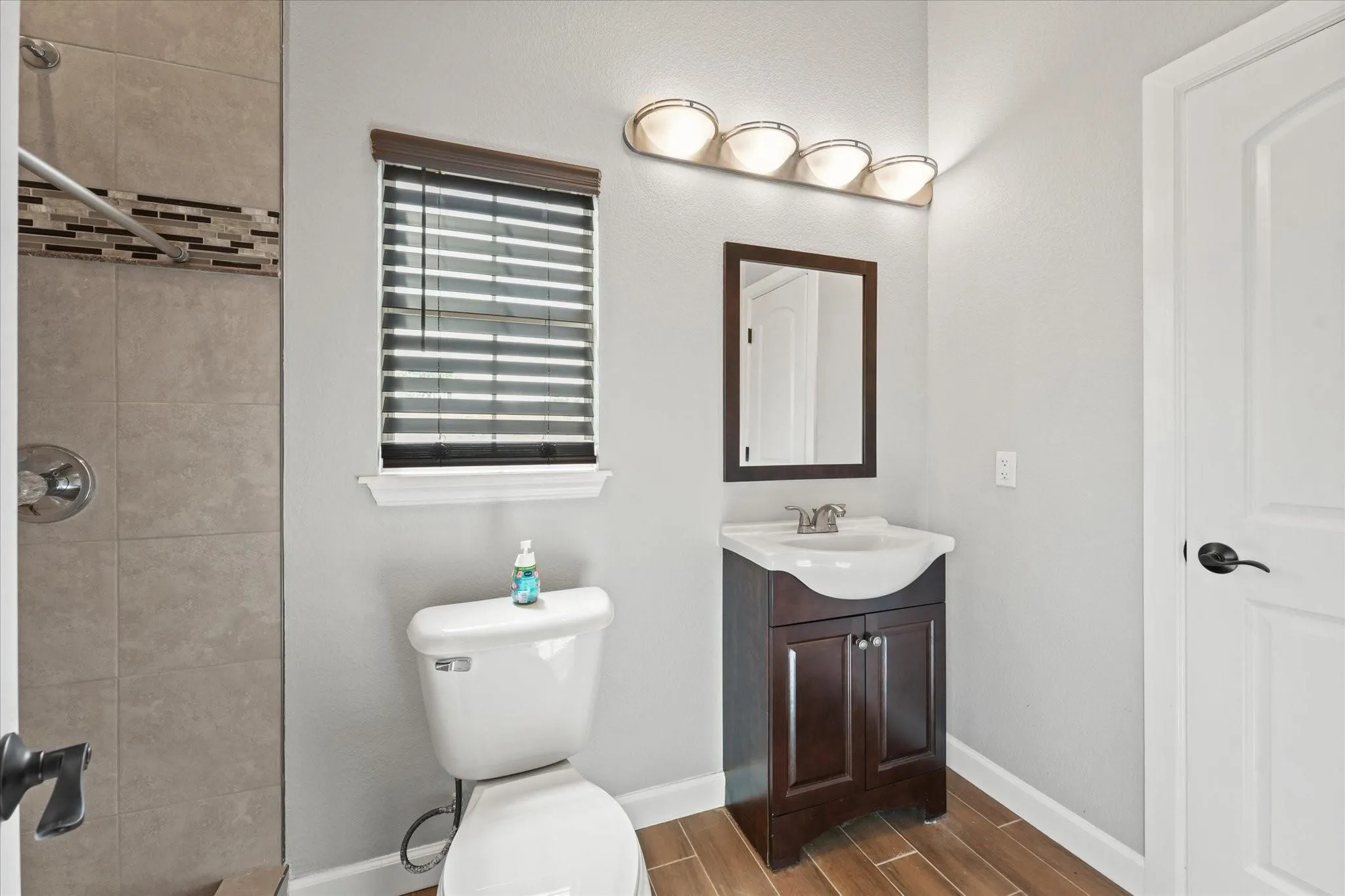 Bathroom featuring a dark wood-finish vanity with an integrated sink, framed mirror, and a four-bulb vanity light fixture