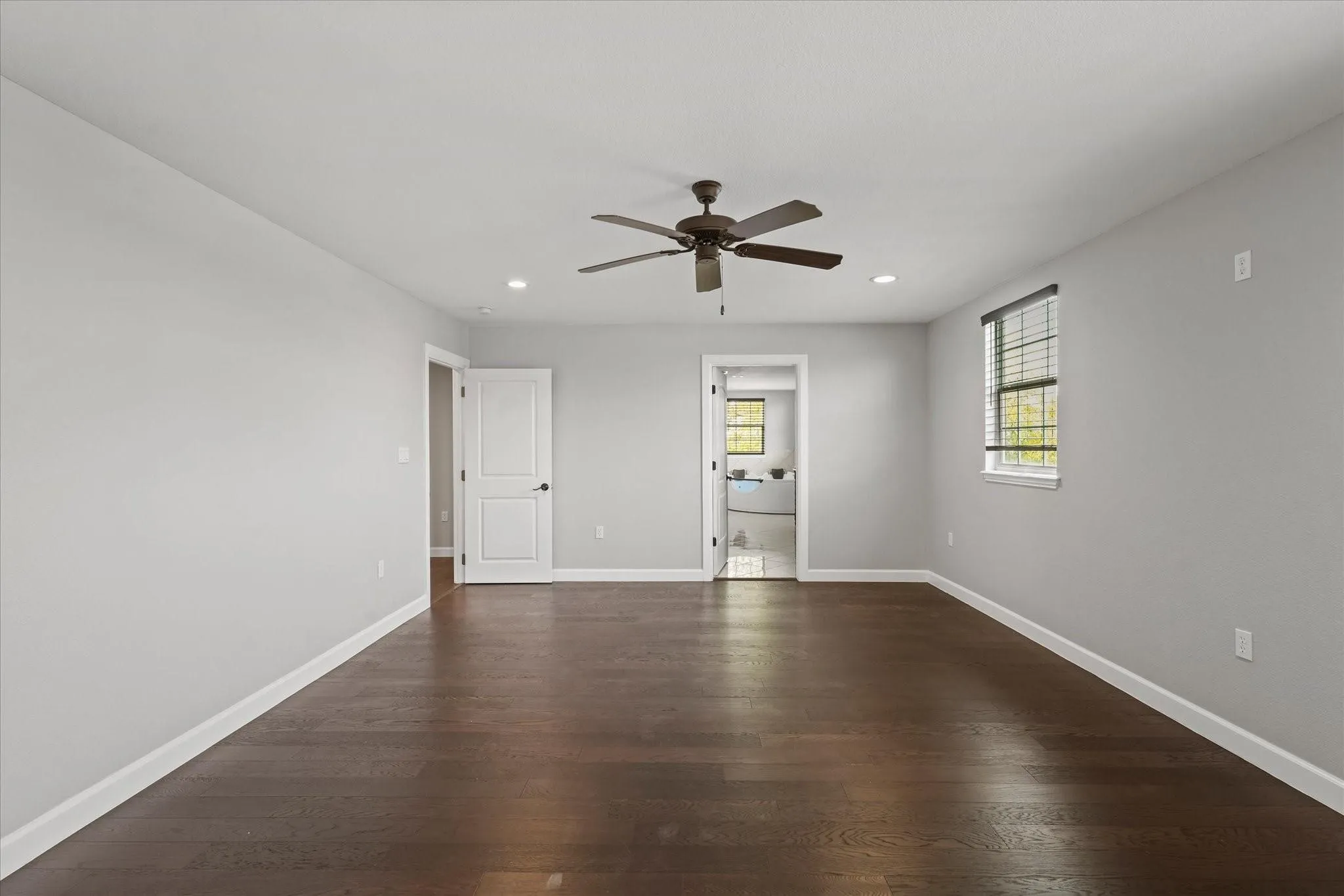 Spacious room featuring dark wood-finish flooring, light gray walls, and white baseboards