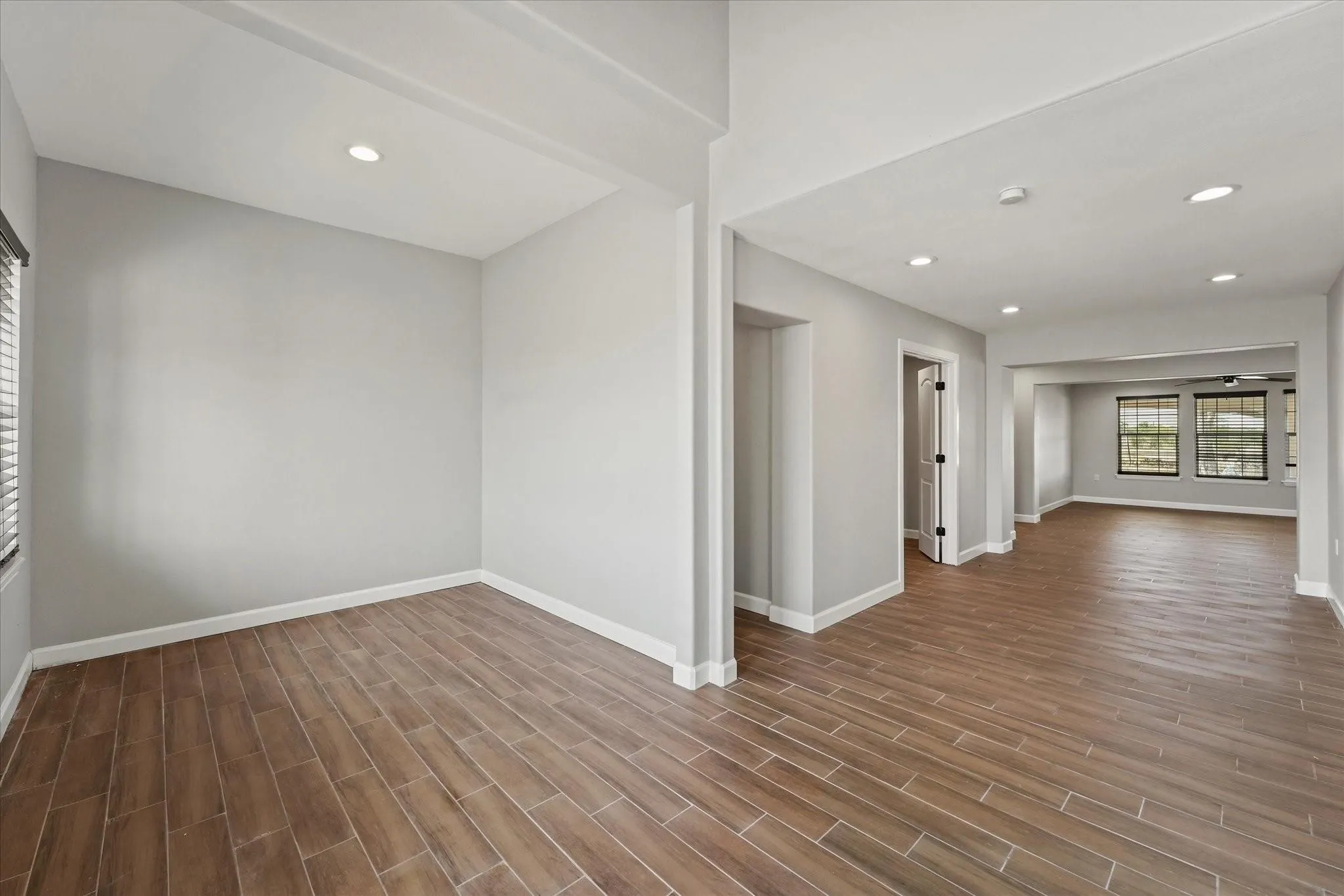 Open-concept living area featuring wood-finish plank tile flooring throughout, recessed lighting, neutral wall tones, and white baseboards