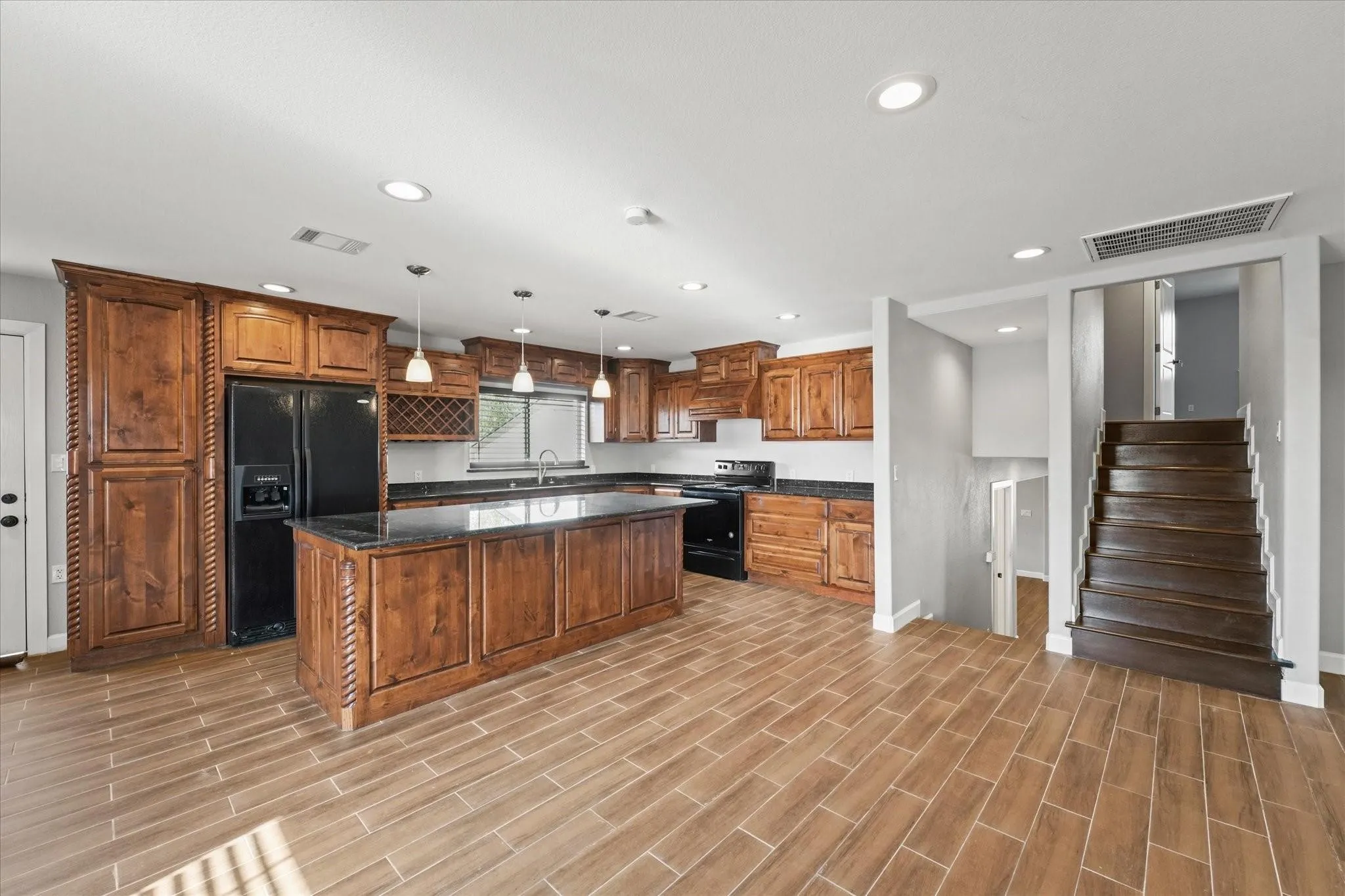 Open-concept kitchen featuring wood-finish flooring, dark wood cabinetry, black appliances, and dark countertops