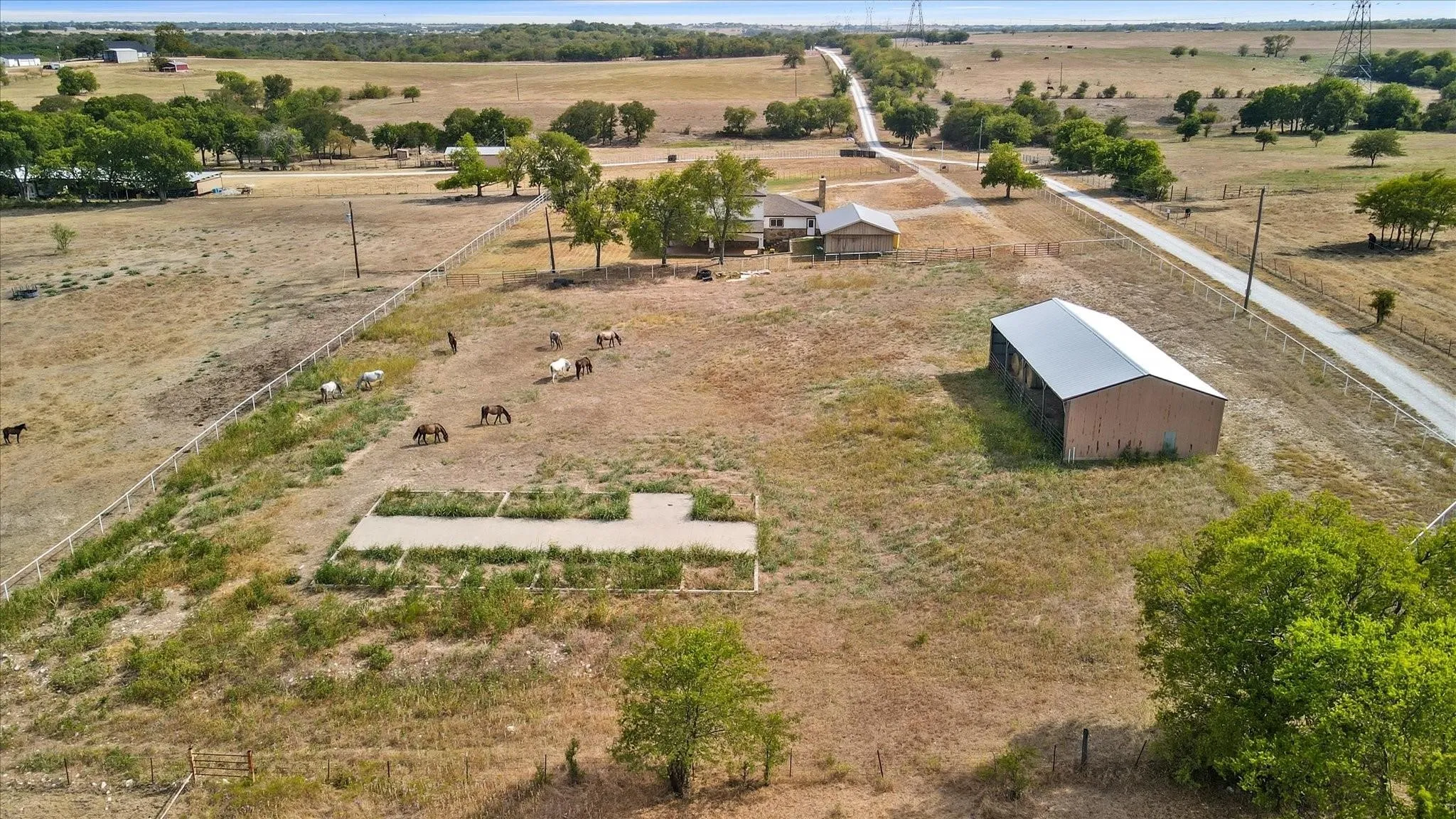 Expansive rural property featuring an open field, a two-story residence, and a large metal barn with a light-colored roof