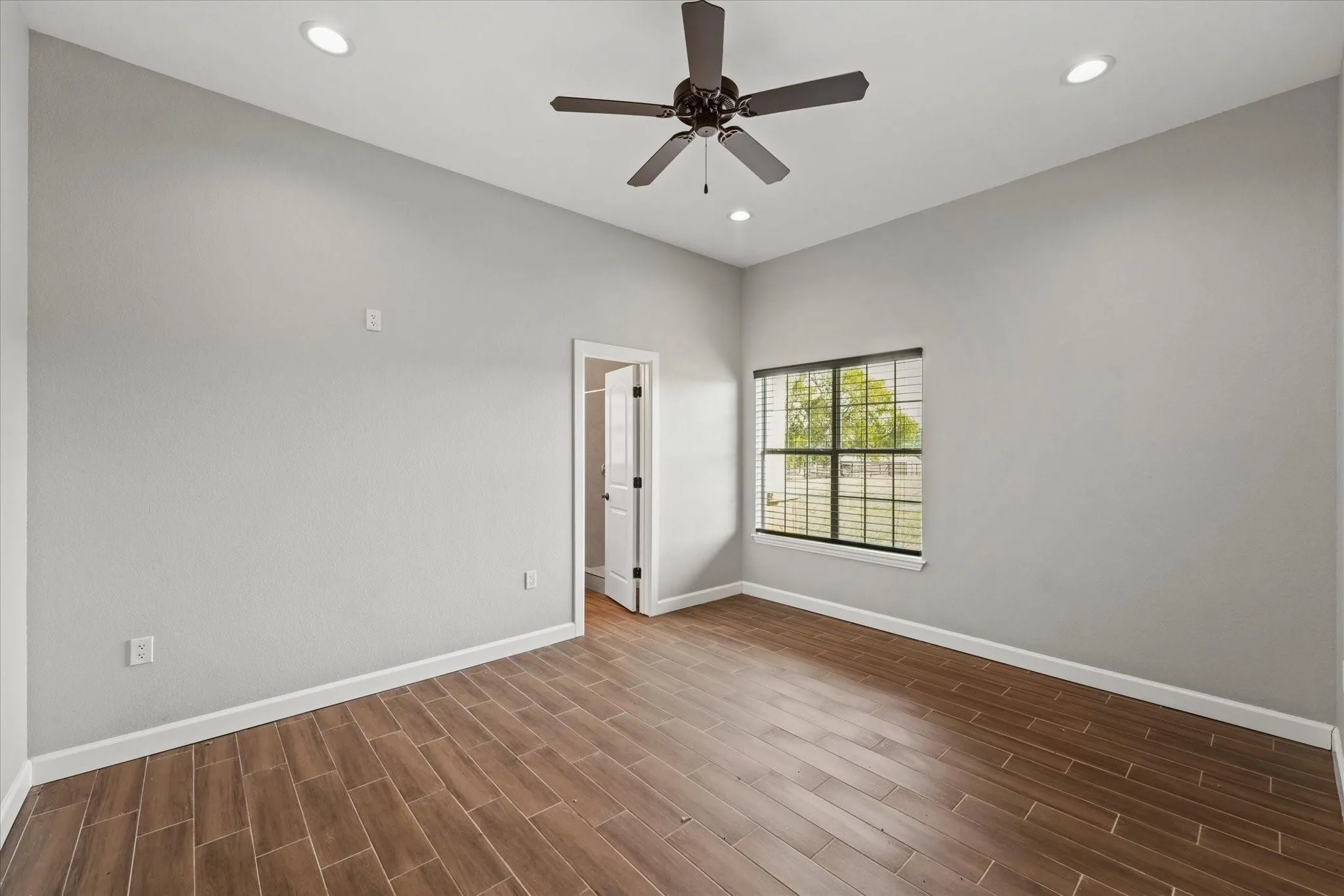 Interior room featuring wood-finish tile flooring, a dark-toned ceiling fan, recessed ceiling lighting, a window with blinds, and a white interior door