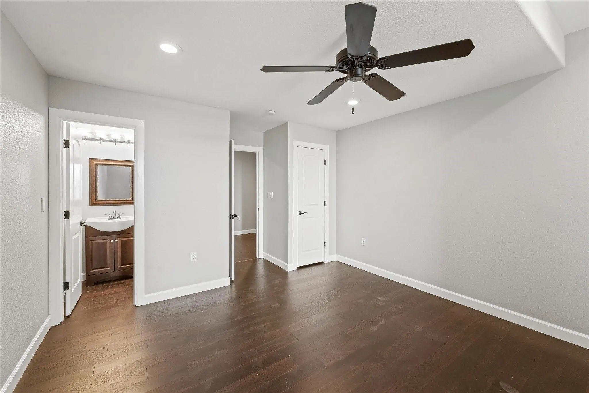 Spacious room featuring dark wood-finish flooring, light gray walls, white trim, and a ceiling fan with integrated lighting
