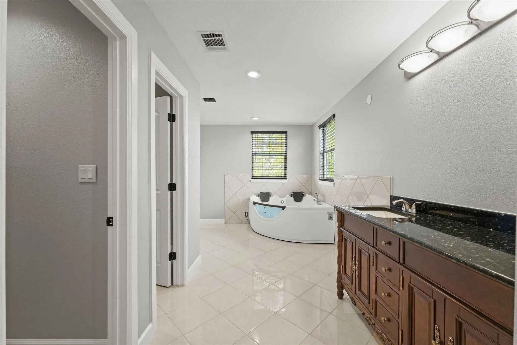 Spacious bathroom featuring a built-in jetted tub, dark wood vanity with a stone countertop, and tile flooring