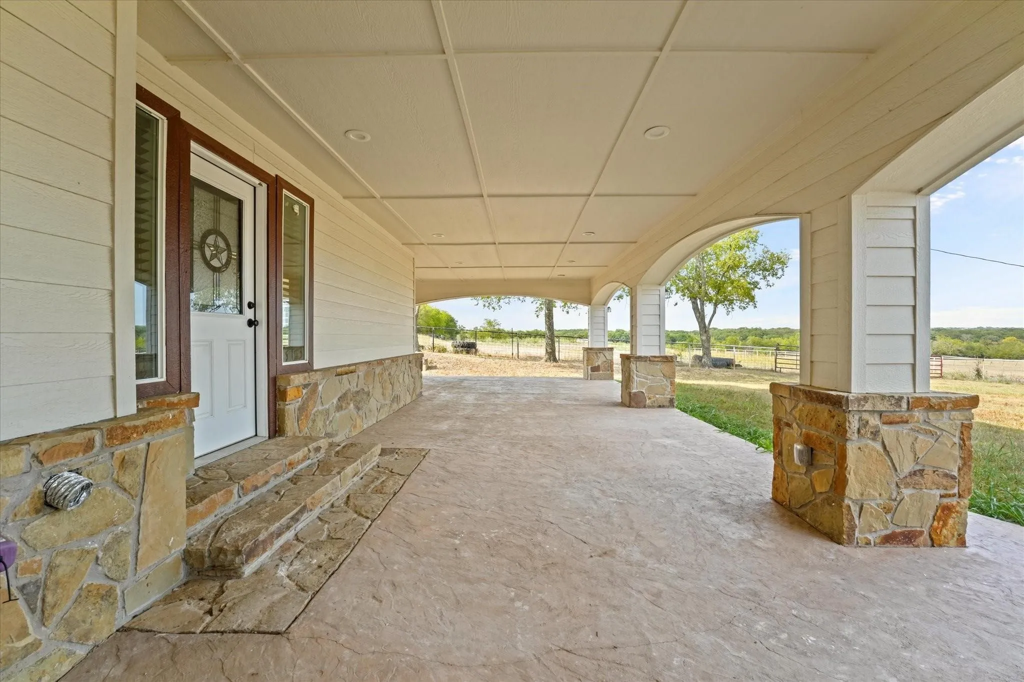 Expansive covered porch featuring a stamped concrete floor, stone veneer accents, recessed lighting, and board and batten siding