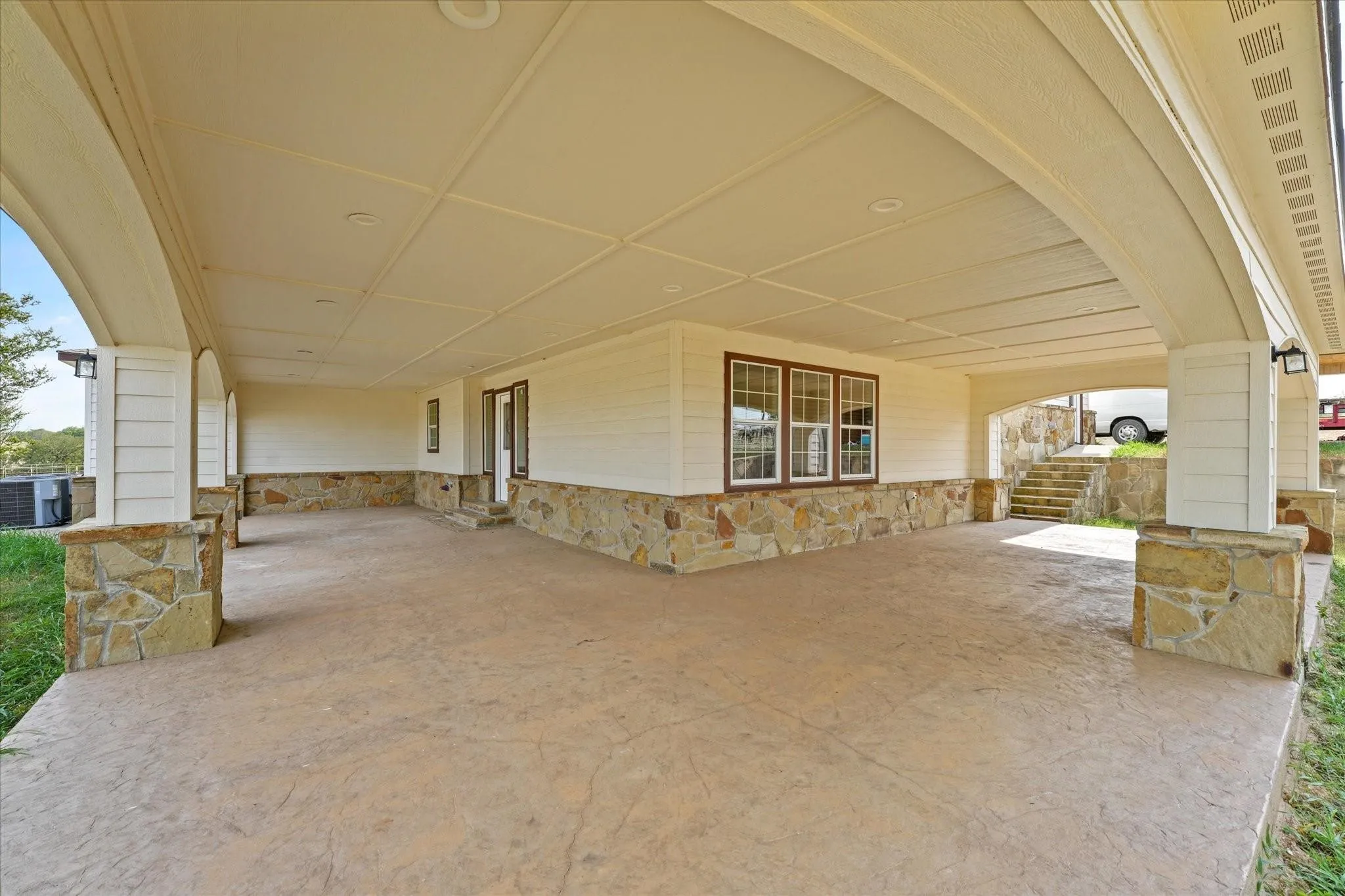 Expansive covered patio featuring a stamped concrete surface, stone accents, recessed lighting, and direct exterior access