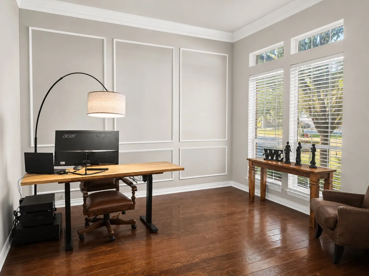 Neutral wall color with applied wall molding, dark wood-finish flooring, and large windows with transom lighting