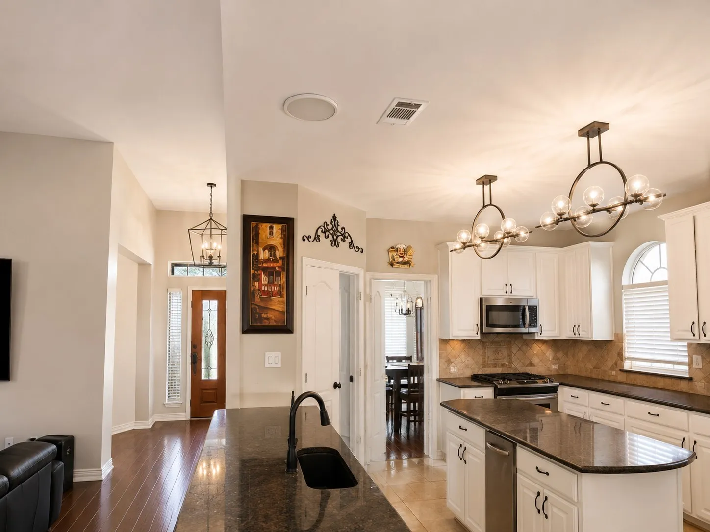 Gourmet kitchen with an expansive granite island, stainless steel appliances, white cabinetry, and decorative pendant lighting
