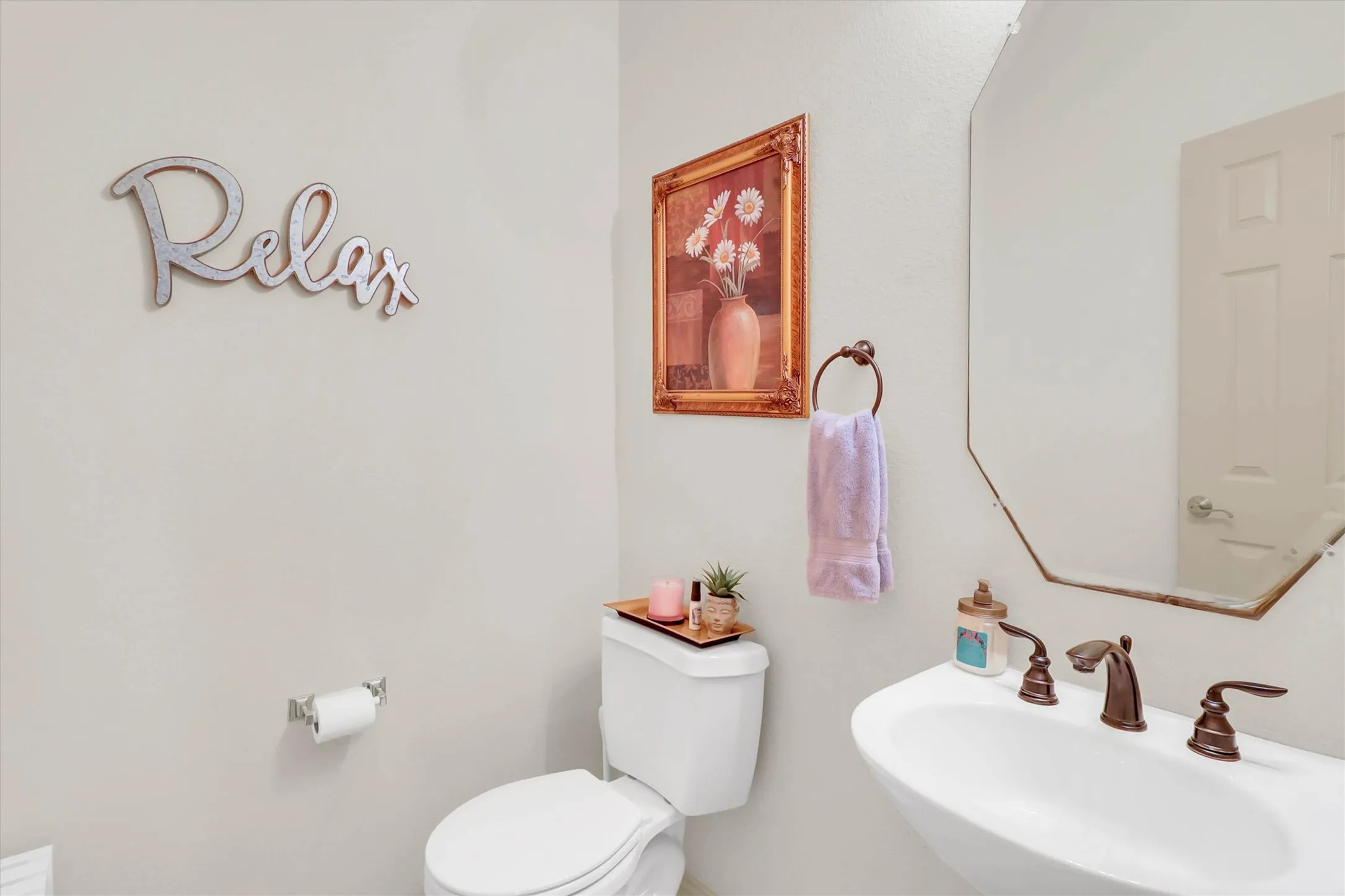 Powder room featuring a pedestal sink with bronze-finish faucet, a toilet, and an octagonal mirror