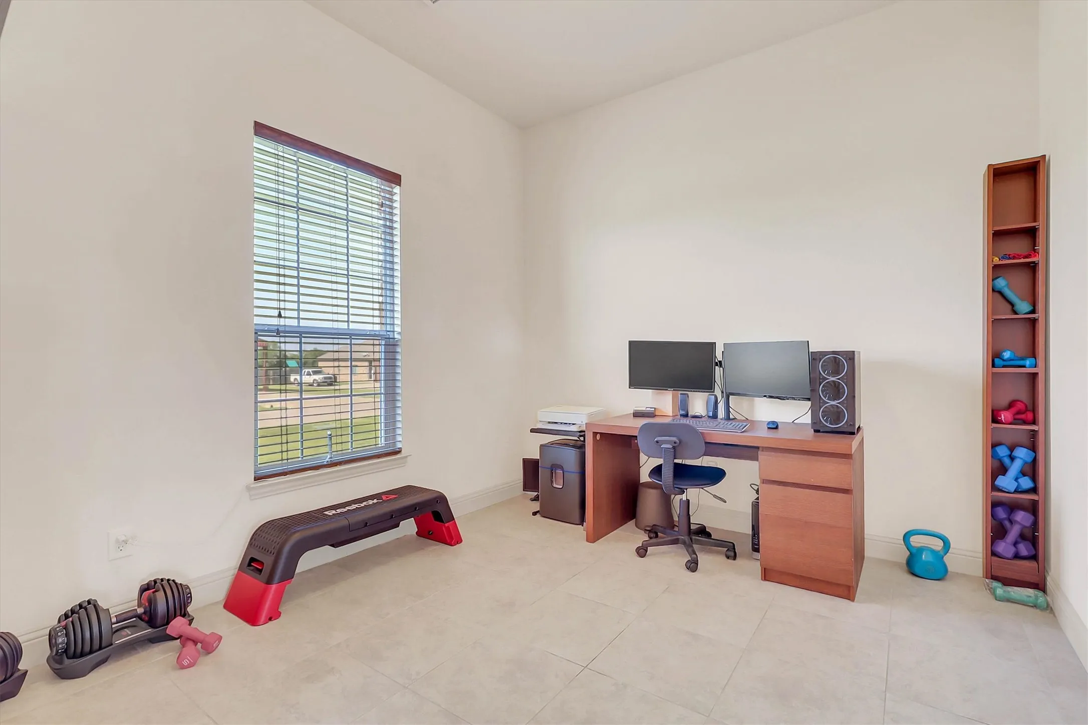 Room featuring neutral wall tones, tile flooring, a window with blinds, and a built-in vertical shelving unit