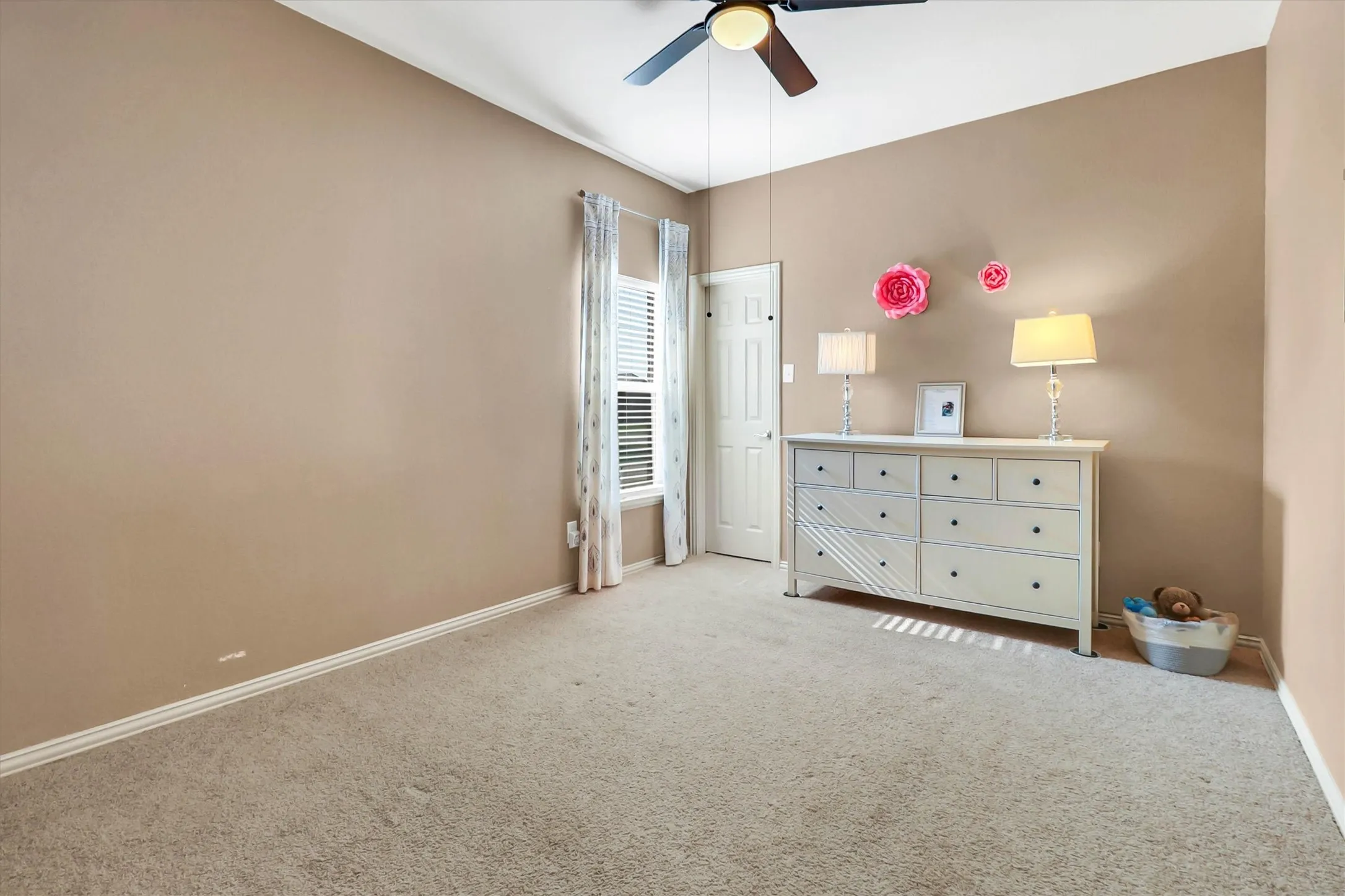 Carpeted interior room with neutral-toned walls, white baseboards, and a ceiling fan with integrated lighting
