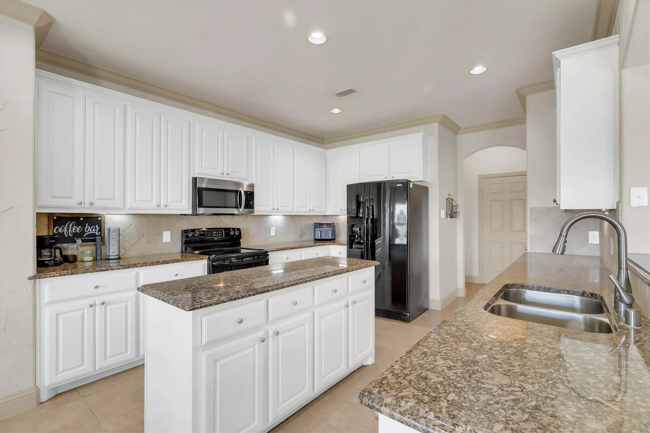 Kitchen featuring white cabinetry, granite countertops, a central island, stainless steel sink, and recessed lighting