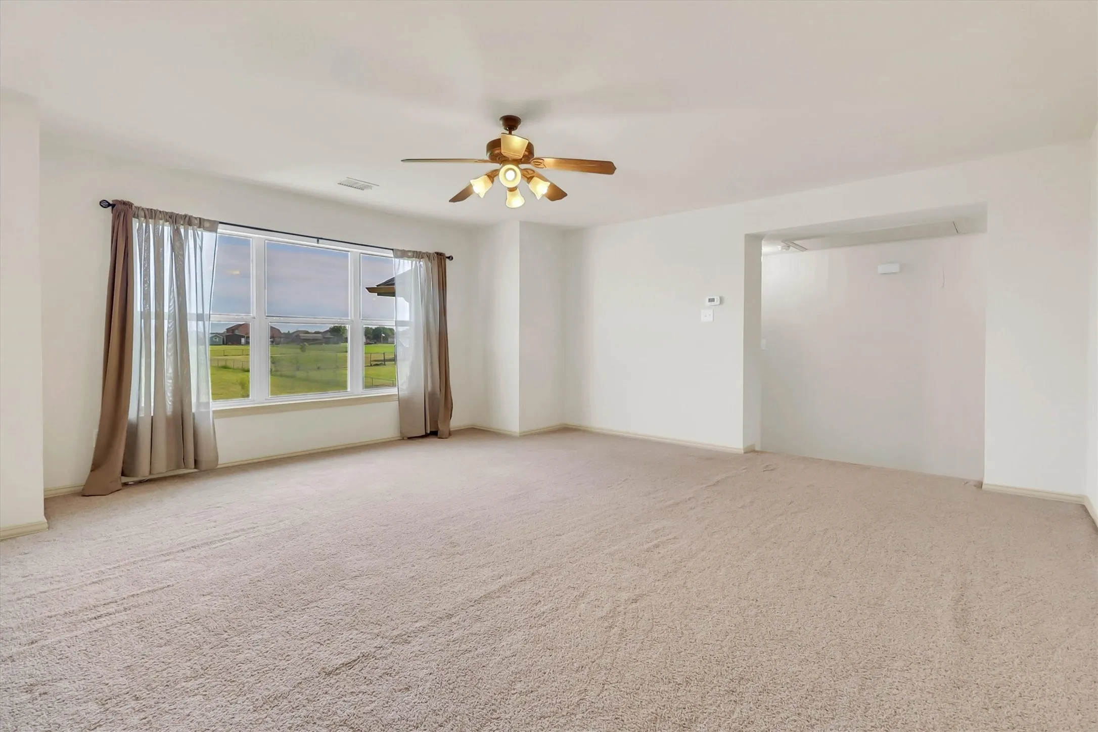 Spacious room featuring neutral carpet flooring, a large multi-pane window, and a ceiling fan with integrated lighting