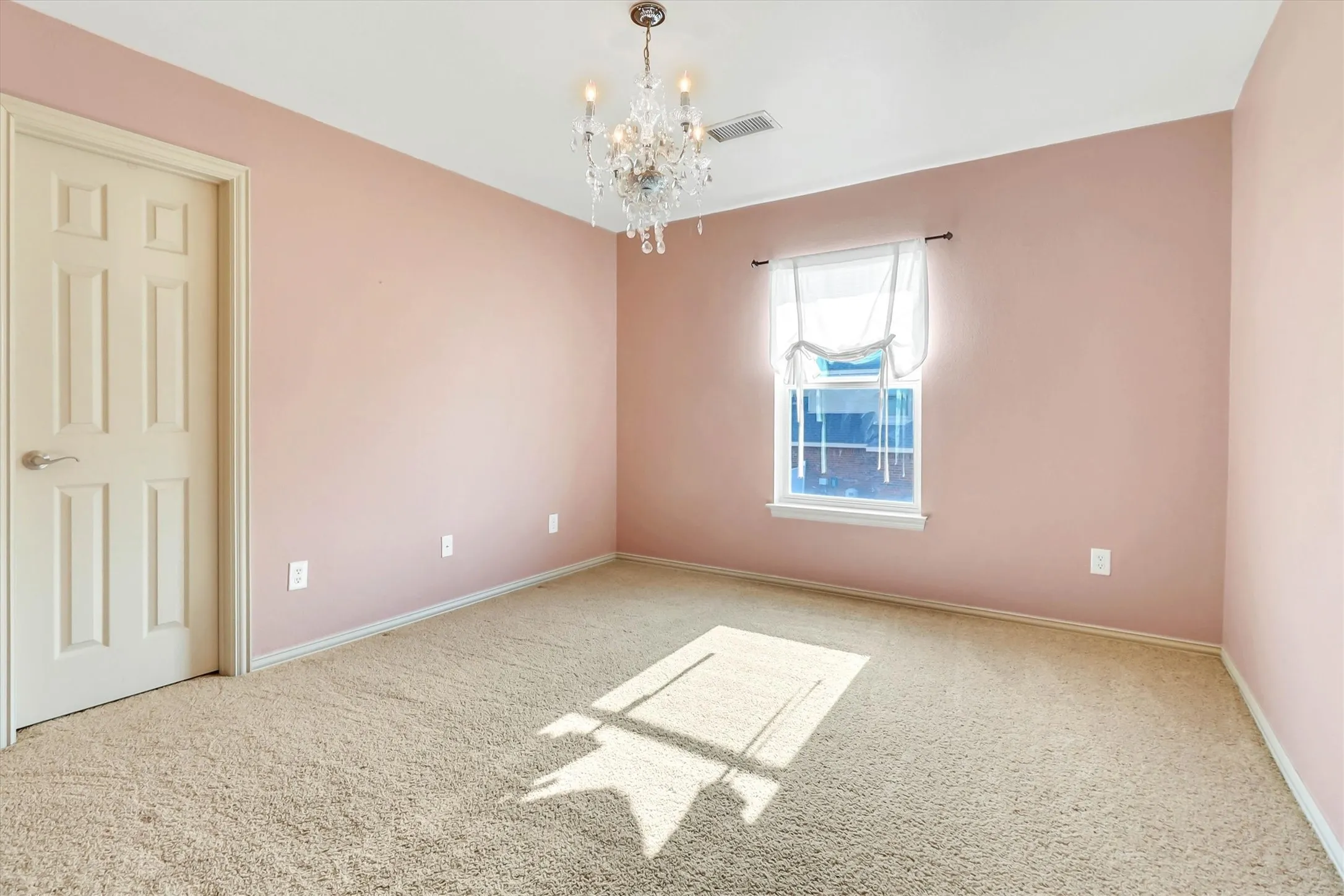 Carpeted interior room featuring a decorative chandelier, single window with white trim, and a paneled interior door