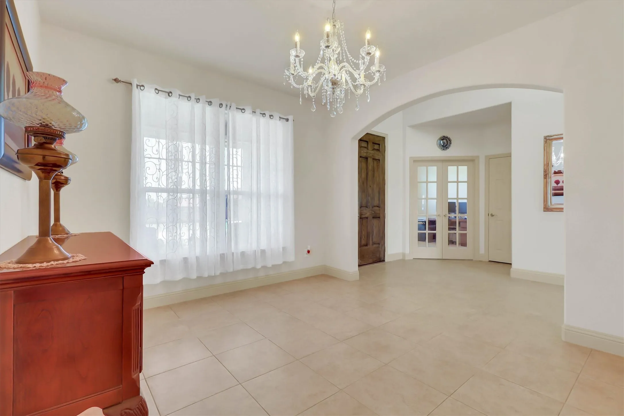 Spacious interior featuring a crystal chandelier, arched entryway, light-toned tile flooring, and double French doors with glass panes