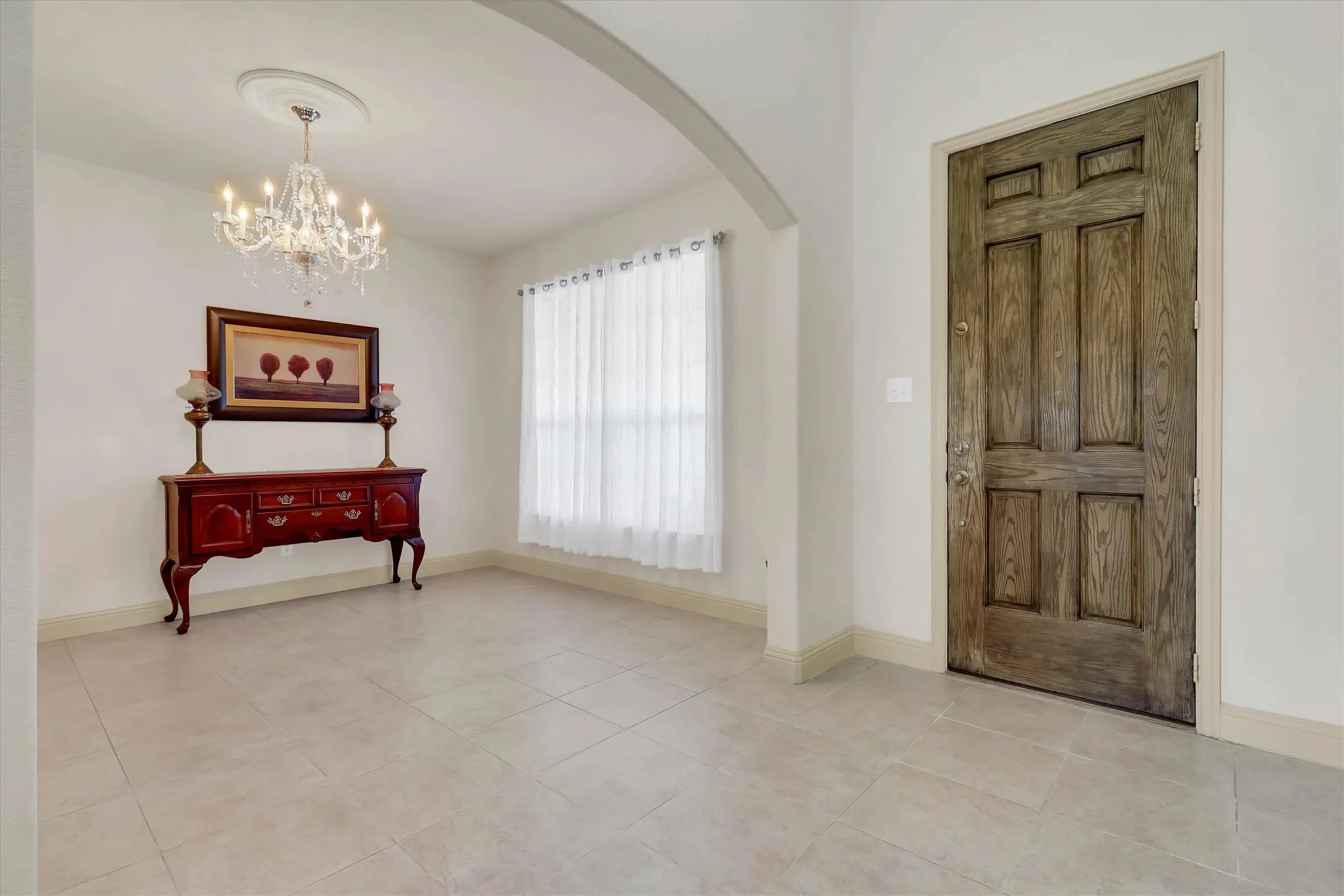 Entryway featuring a paneled wood door, light-colored tile flooring, and an arched doorway