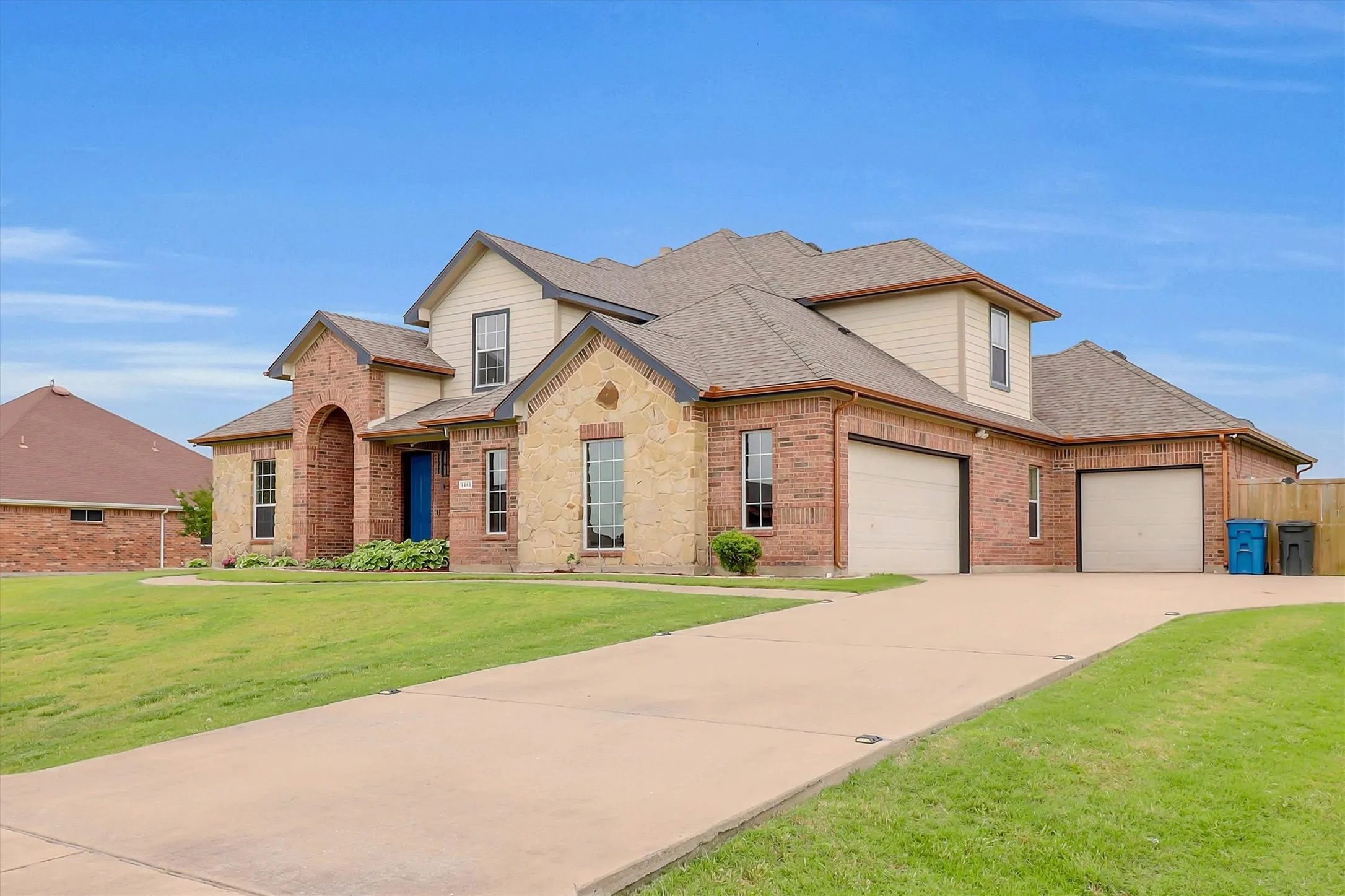 Brick and stone facade residence featuring a prominent arched entry, two attached garages, and a concrete driveway