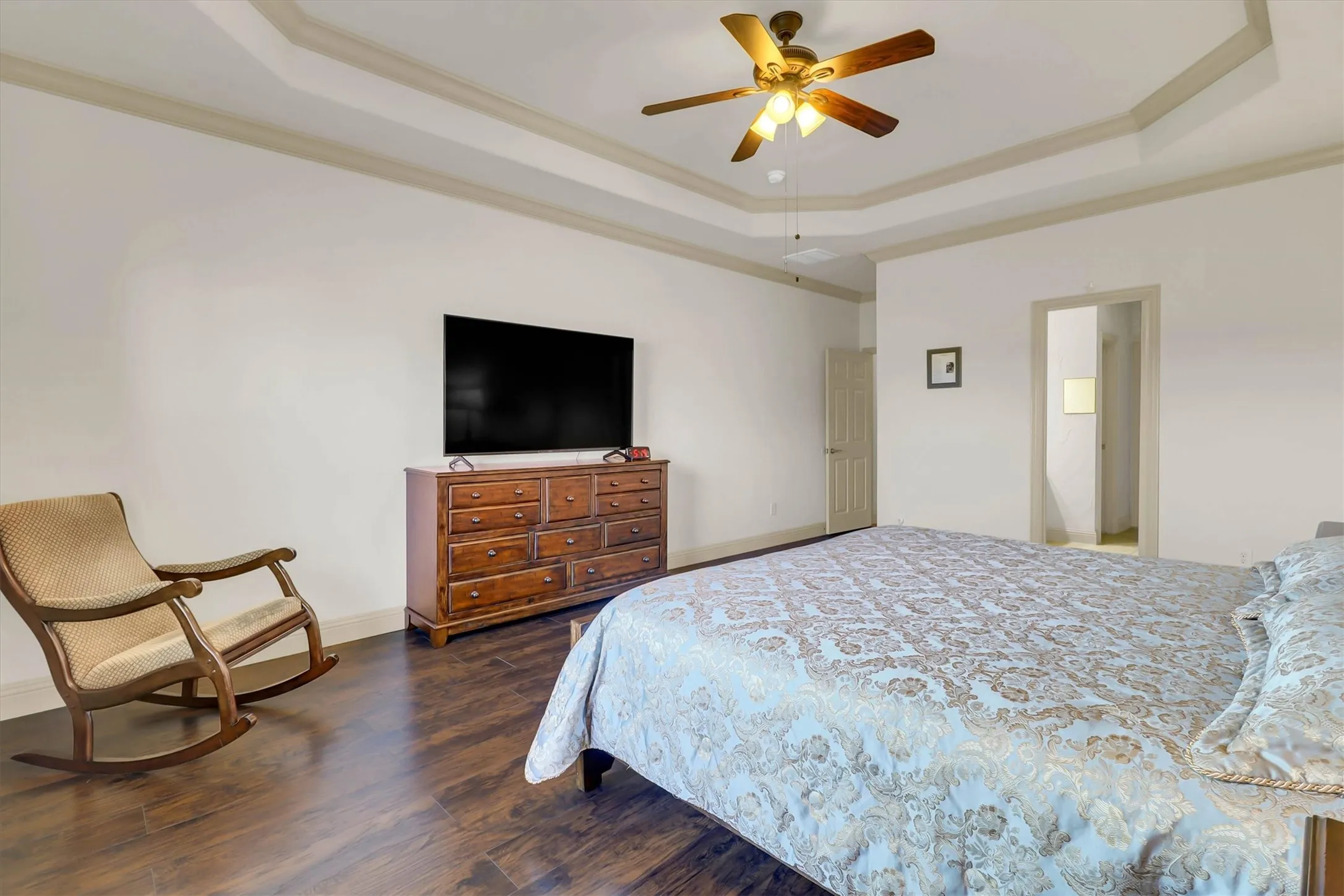Spacious room featuring wood-finish flooring, a tray ceiling with crown molding, and a ceiling fan with integrated lighting