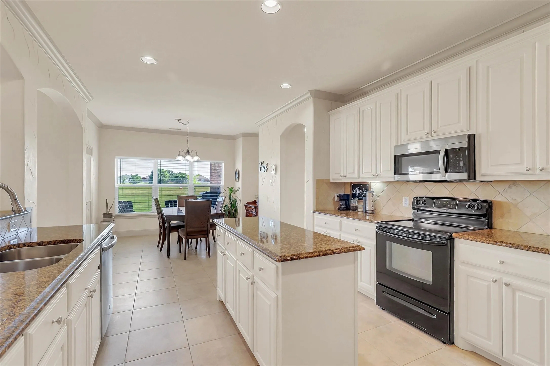 Open-concept kitchen featuring white cabinetry, granite-finish countertops, and stainless steel appliances