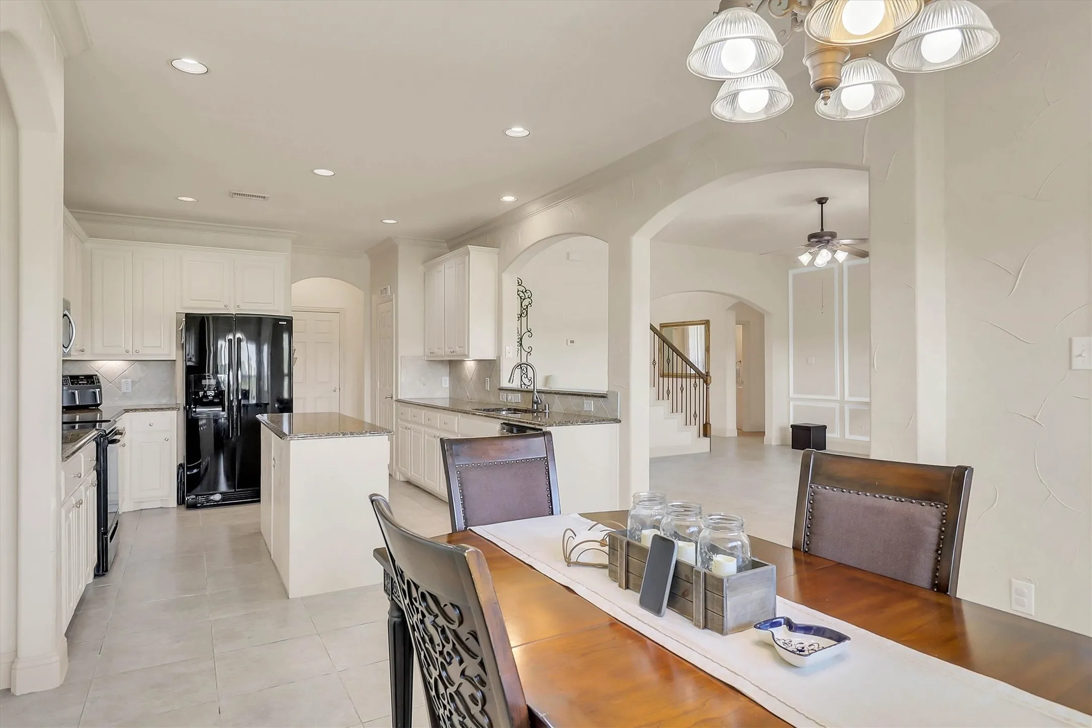 Open-concept kitchen featuring white cabinetry, granite countertops, a central island, and tile flooring