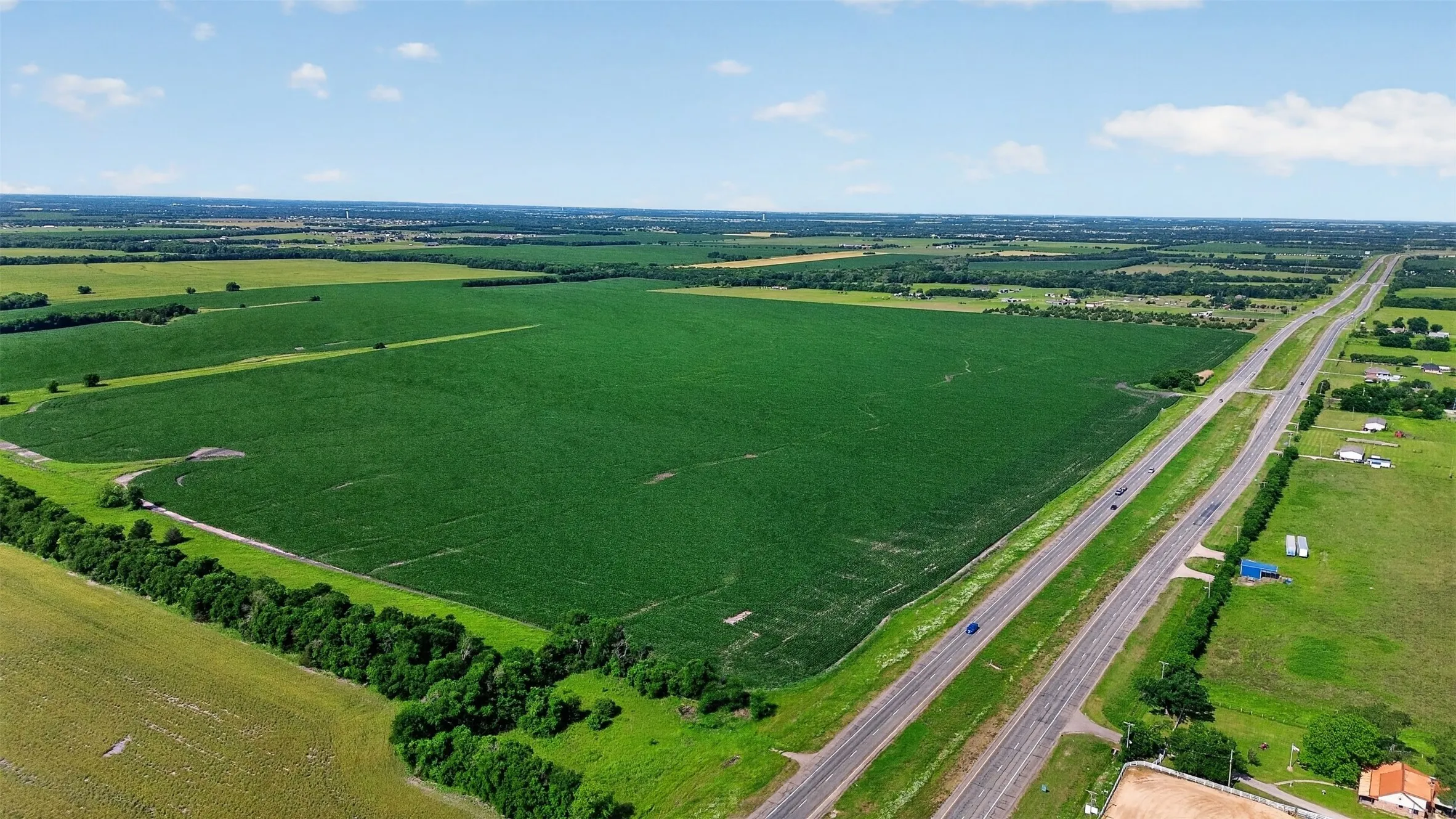 Expansive agricultural land featuring cultivated fields, green pastures, and mature tree lines