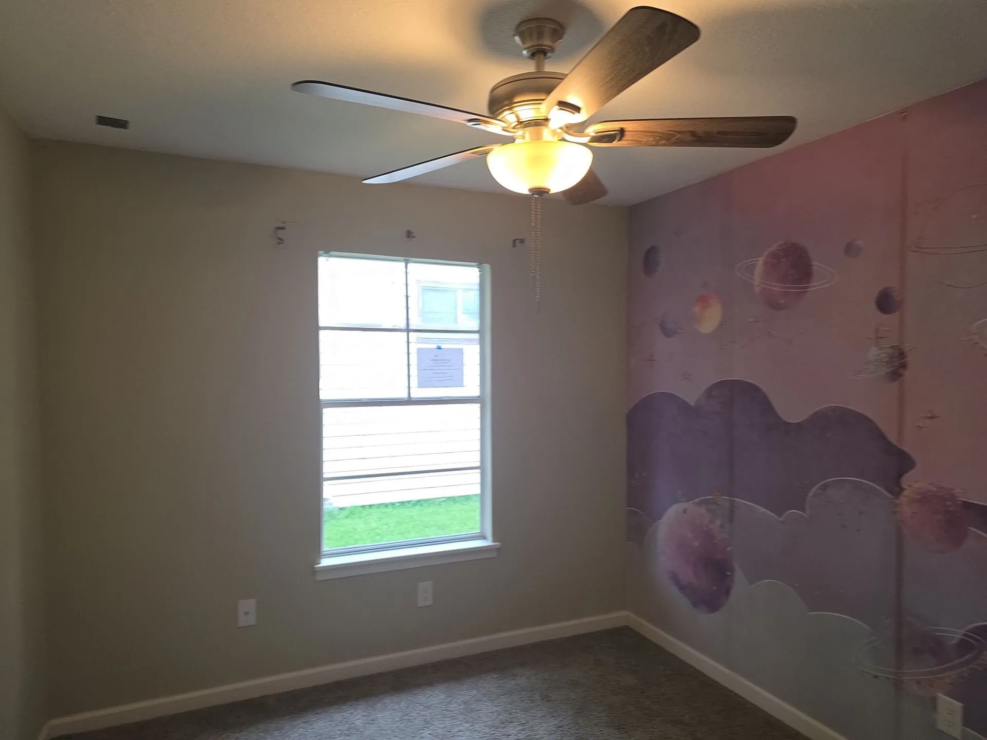 Room featuring a ceiling fan with light fixture, large window, and patterned accent wall