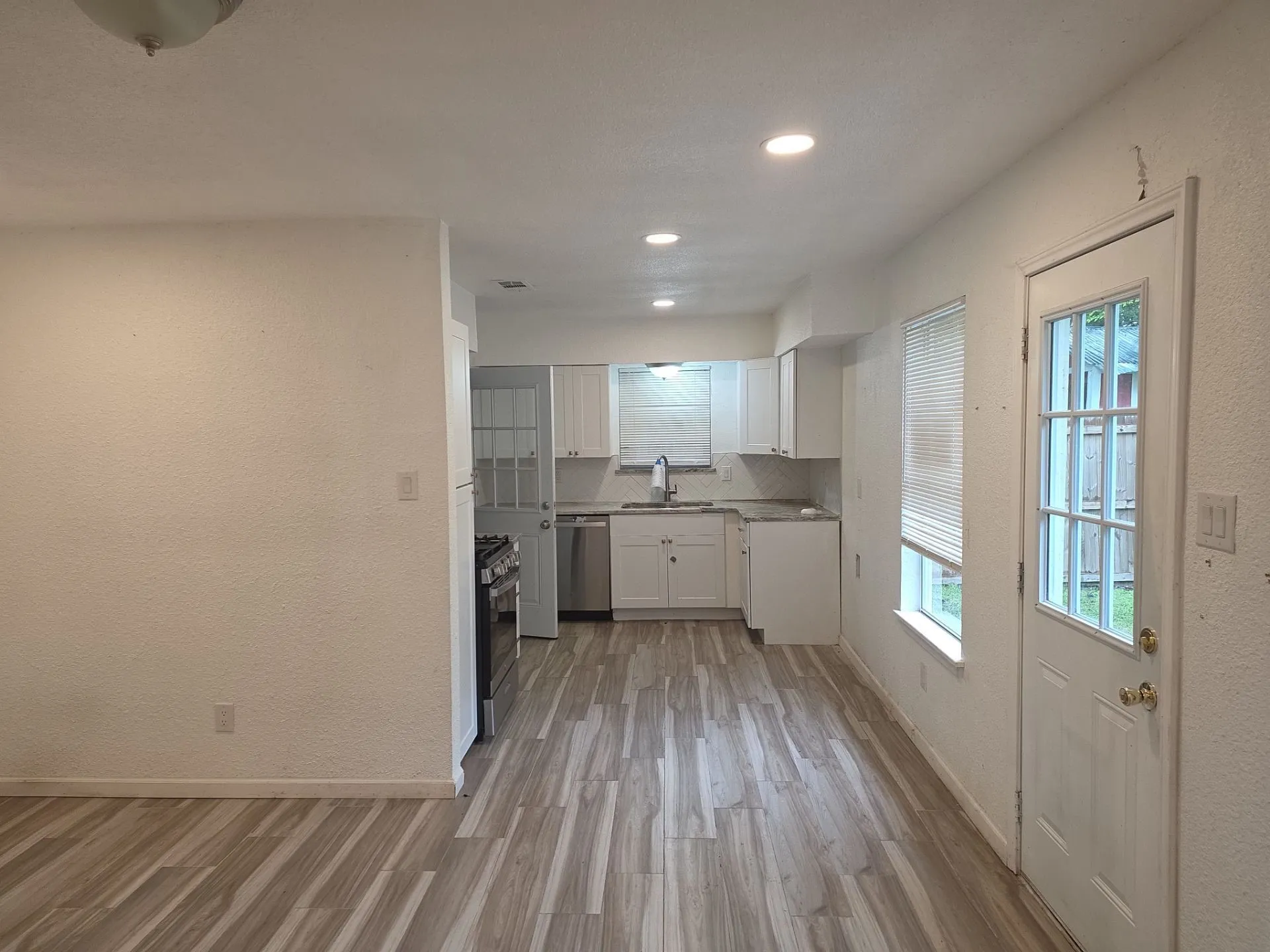Open-concept kitchen featuring wood-finish flooring, white cabinetry, recessed lighting, stainless steel appliances, and a glass-paned exterior door