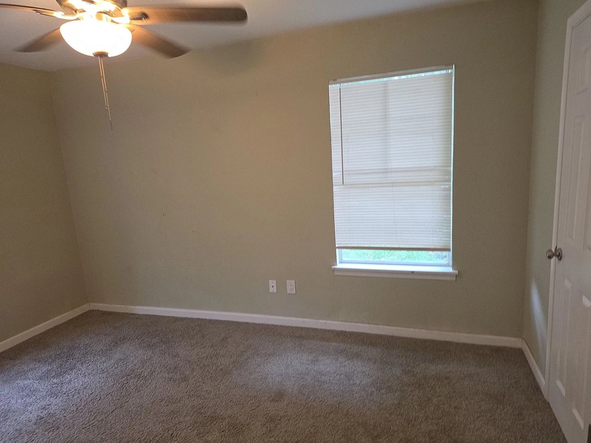 Carpeted room featuring a ceiling fan with integrated lighting, a window with horizontal blinds, and a white paneled door