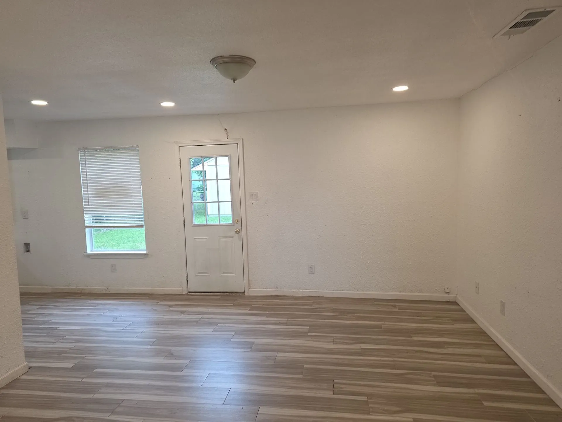 Bright interior space featuring wood-finish flooring, a window with horizontal blinds, and a paneled exterior door with glass inserts