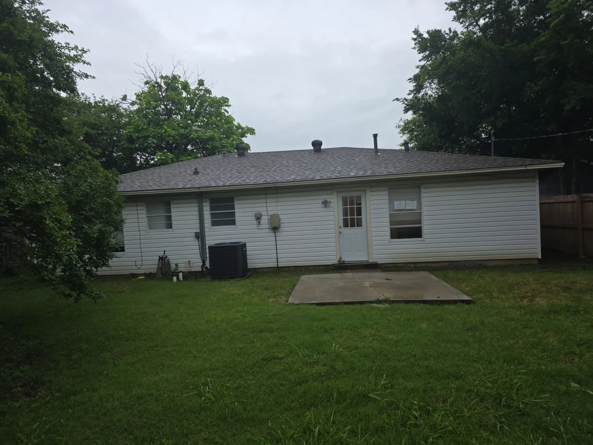 Rear exterior featuring white vinyl siding, a gray shingle roof, and a concrete patio pad