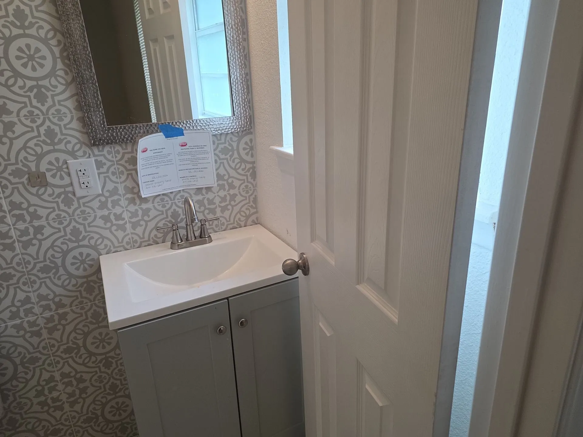 Pedestal sink with a brushed nickel faucet, a textured mirror, and patterned tile wainscoting