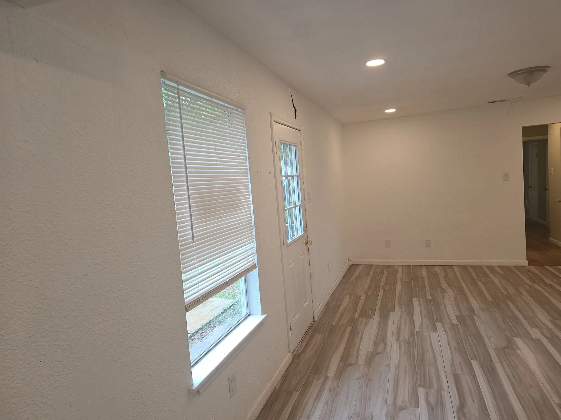 Spacious interior room featuring wood-finish flooring, white walls, and recessed lighting