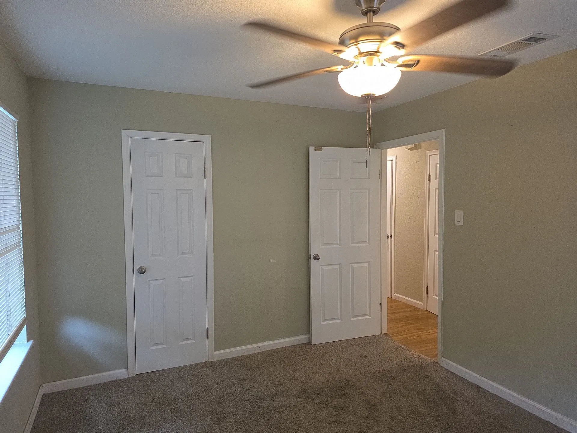 Carpeted room featuring a ceiling fan with integrated lighting, a white six-panel door, and a window with blinds