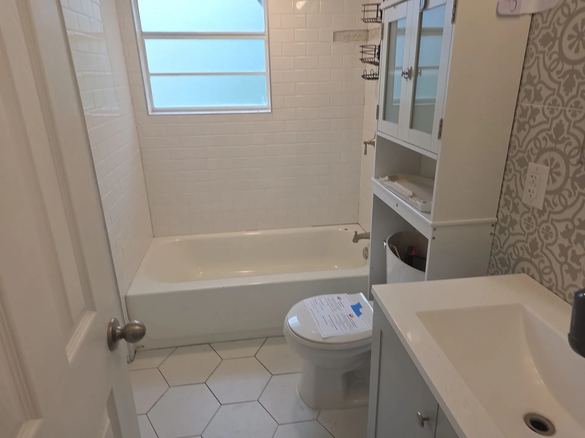 Bathroom featuring a white bathtub with subway tile surround, white hexagonal floor tiles, and a window with obscured glass