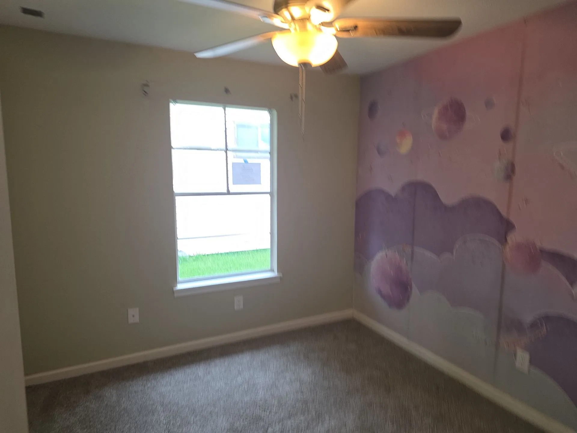 Carpeted room featuring a ceiling fan with light fixture, a window with a white frame, and a wall with a unique mural design