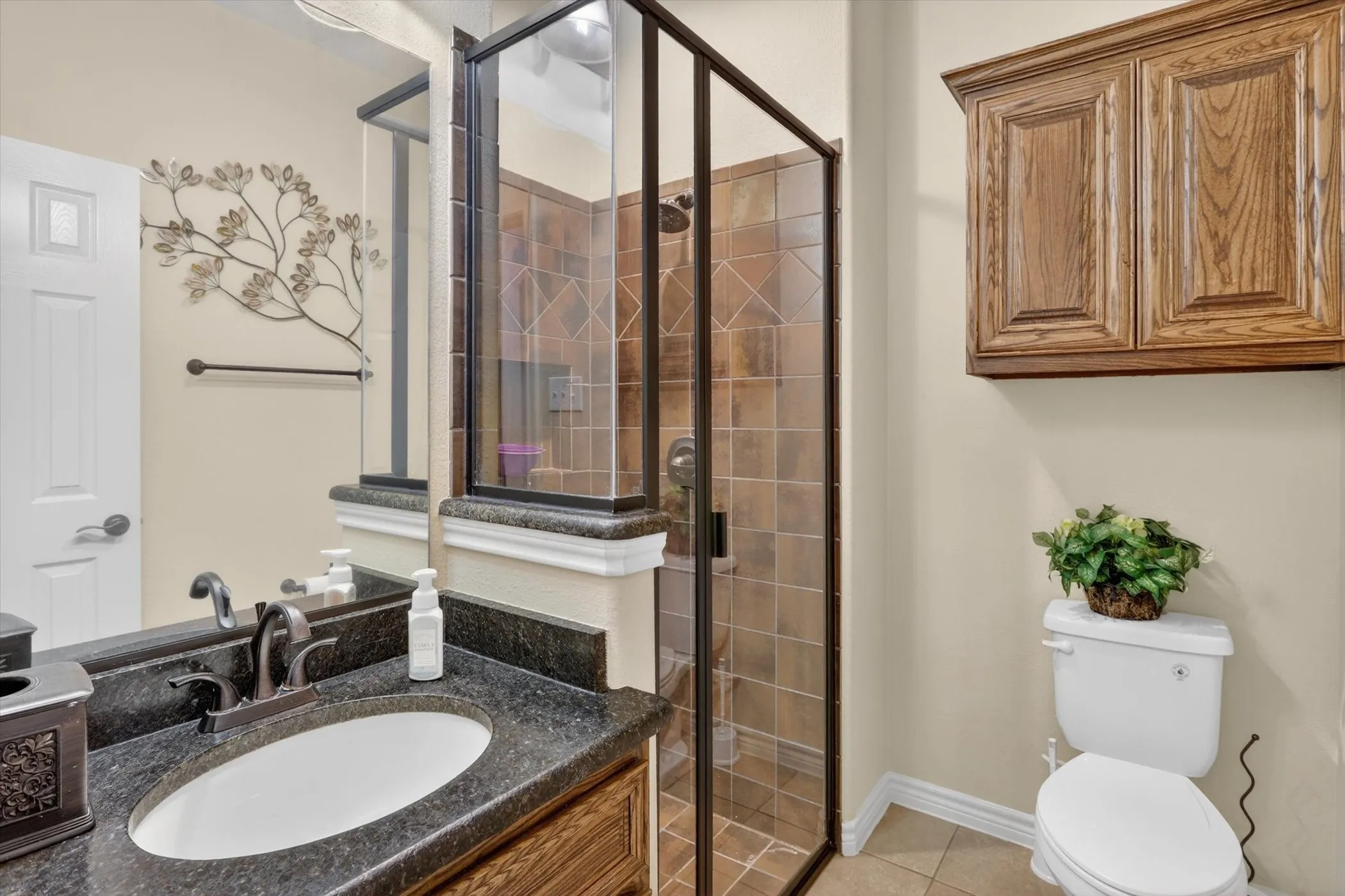 Bathroom featuring a walk-in shower with glass enclosure, a vanity with a dark speckled countertop and undermount sink, and a wood-finish wall-mounted cabinet