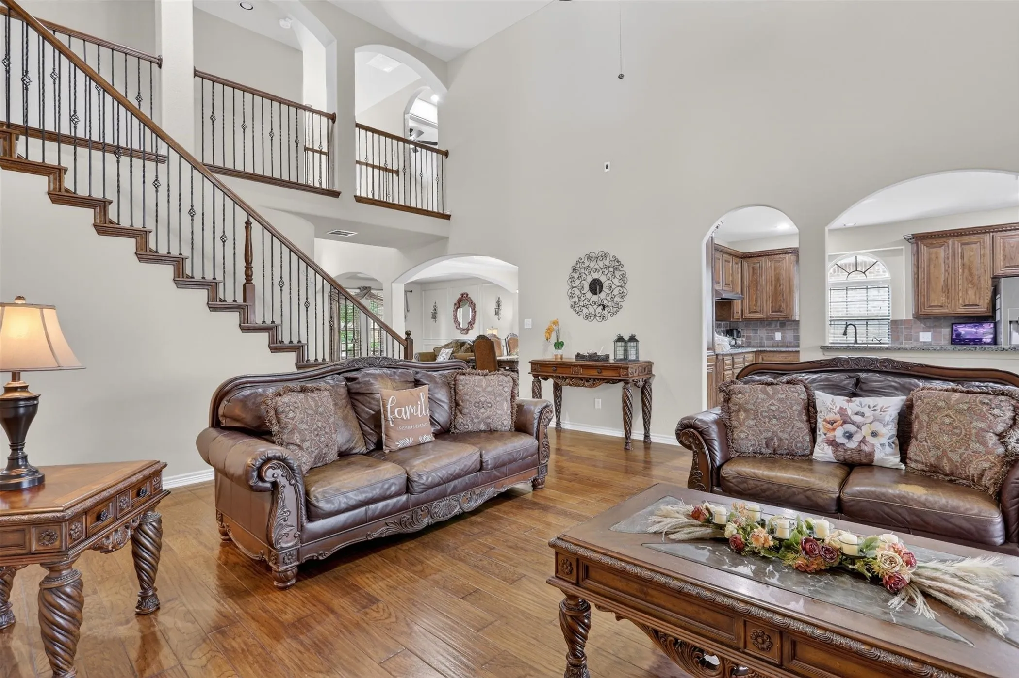 Vaulted ceiling living area featuring wood-finish flooring and a grand staircase with wrought iron balusters