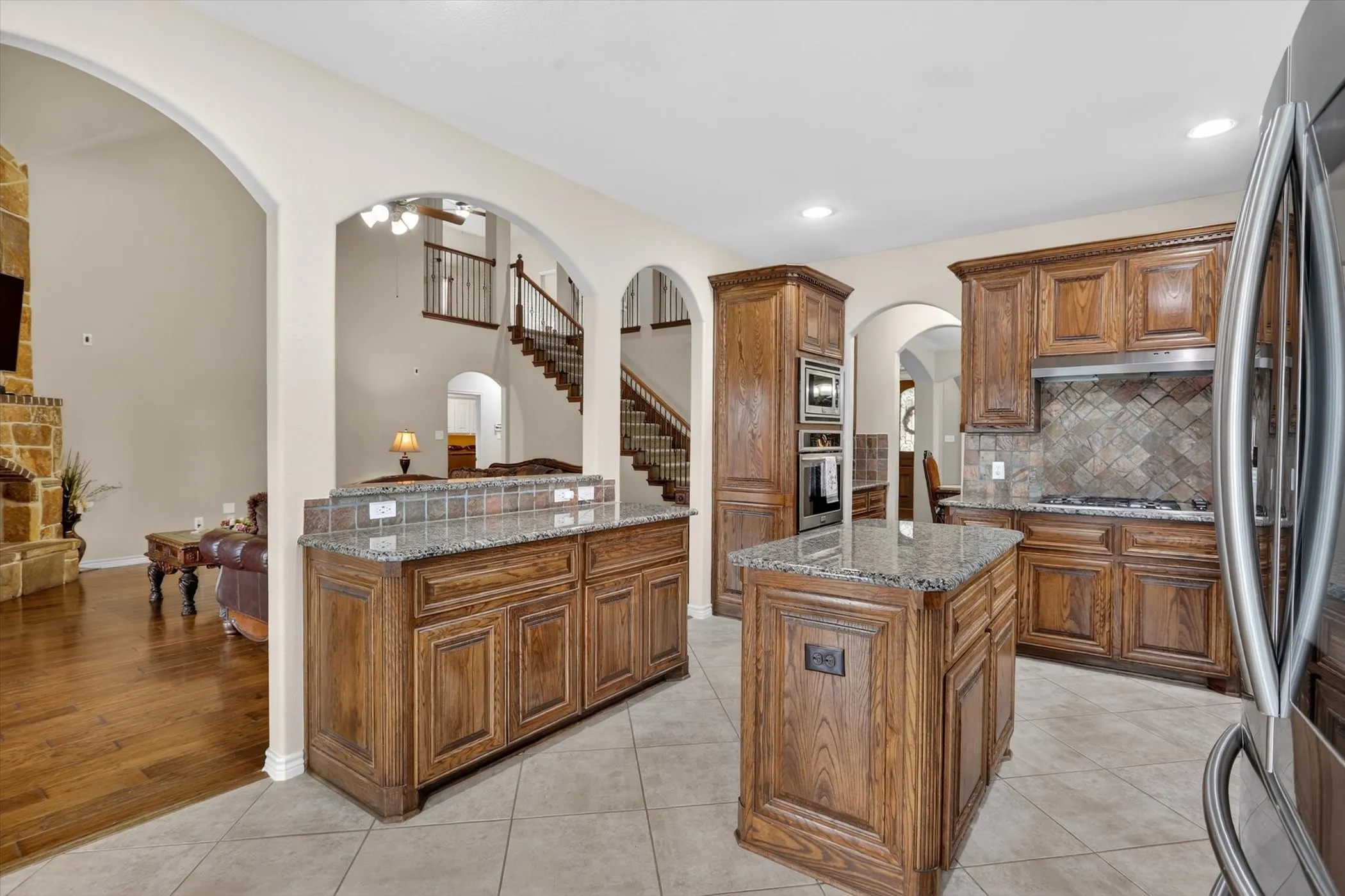 Kitchen featuring extensive wood cabinetry, granite countertops, tile flooring, stainless steel appliances, and a tiled backsplash